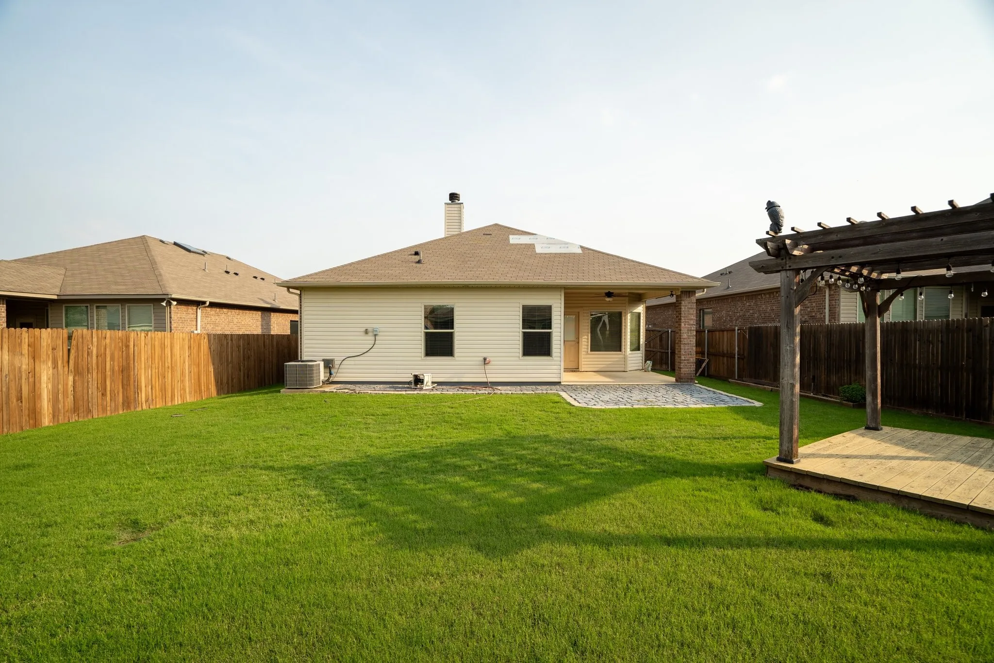Back of property with a pergola, a patio area, central AC unit, and a lawn