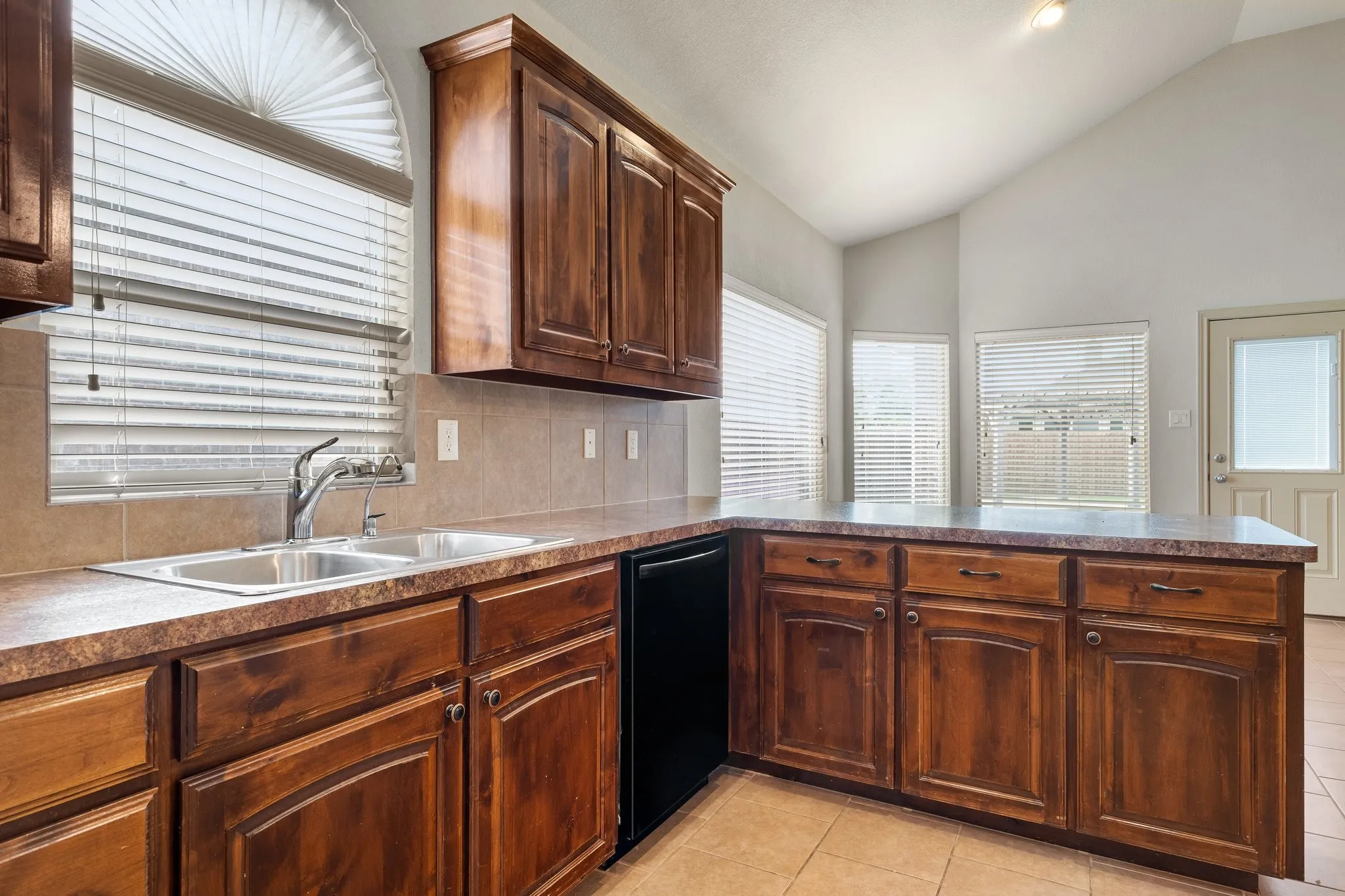 Kitchen with vaulted ceiling, black dishwasher, sink, tasteful backsplash, and light tile floors