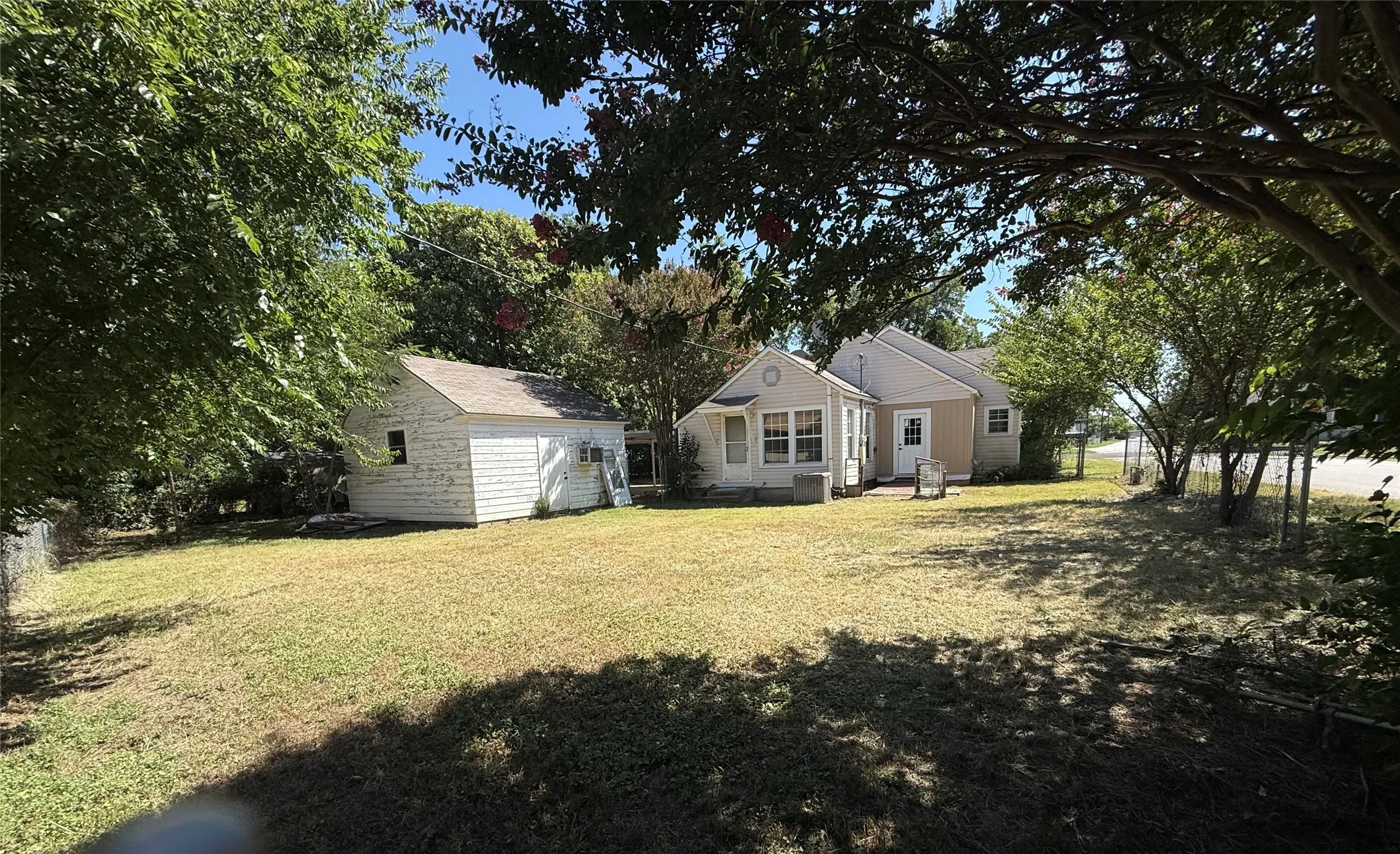 Expansive outdoor space featuring a large lawn, mature trees, and a detached structure with white siding
