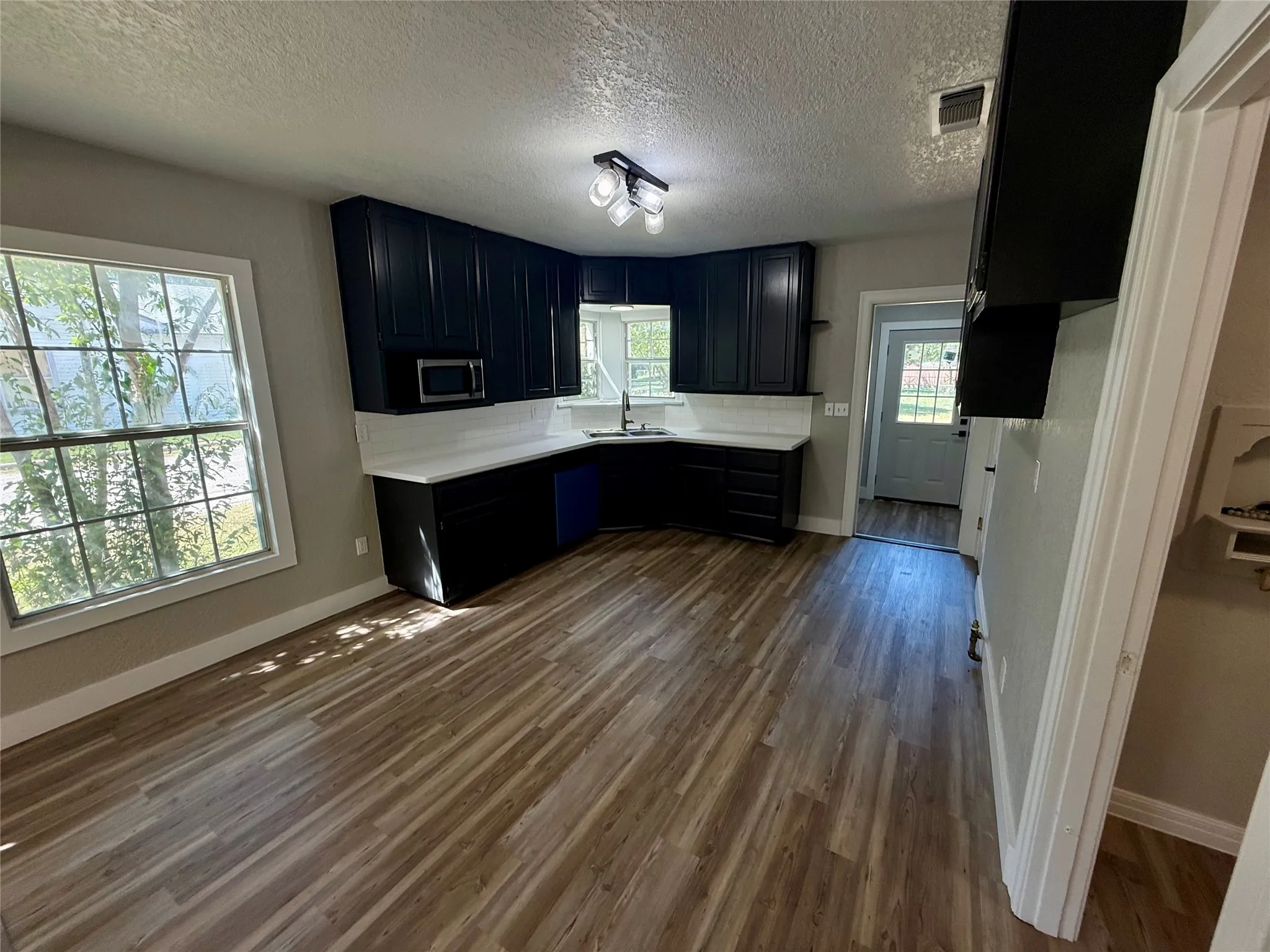 Open-concept kitchen featuring dark cabinetry, white countertops, a tiled backsplash, wood-finish flooring, and a built-in microwave