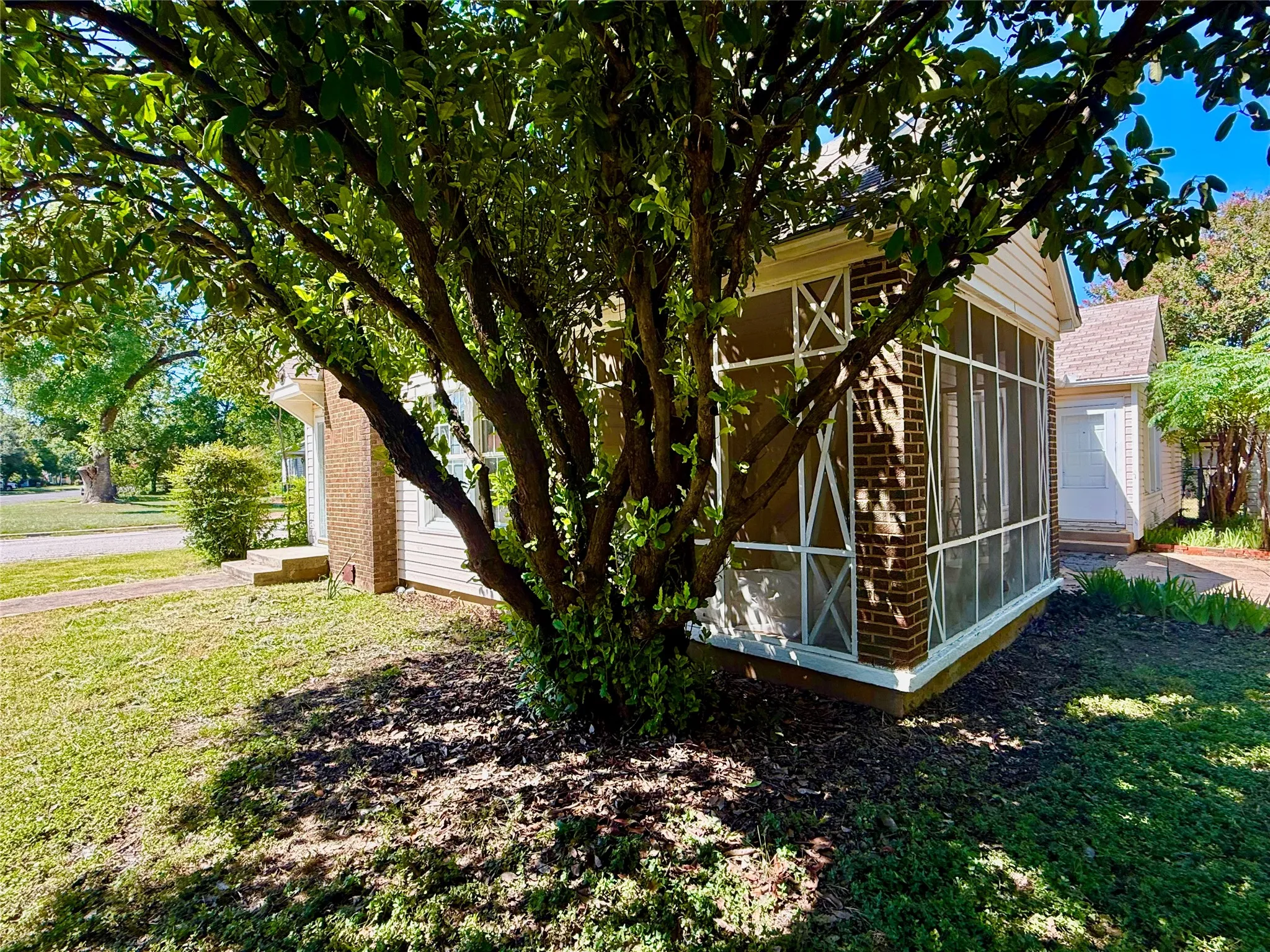 Screened-in porch featuring brick and siding construction, surrounded by mature trees and landscaping