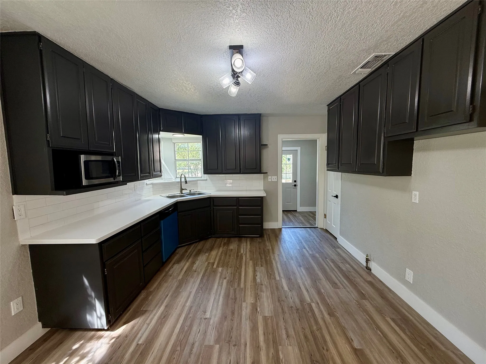 Kitchen featuring extensive dark cabinetry, white countertops, subway tile backsplash, and wood-finish flooring
