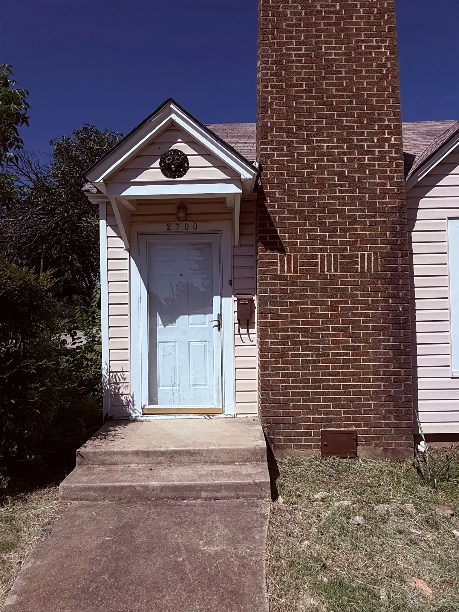 Gable roof entry with decorative vent, concrete porch, and brick chimney