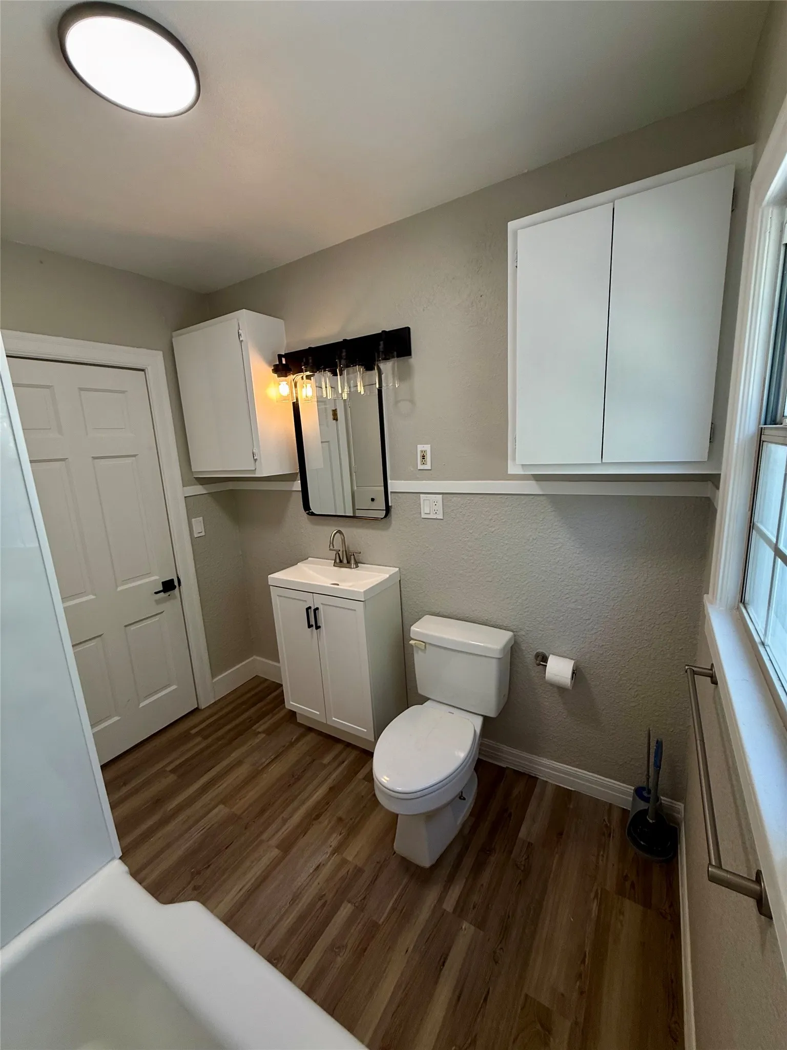 Bathroom featuring a white vanity with integrated sink, wood-finish flooring, and two wall-mounted storage cabinets