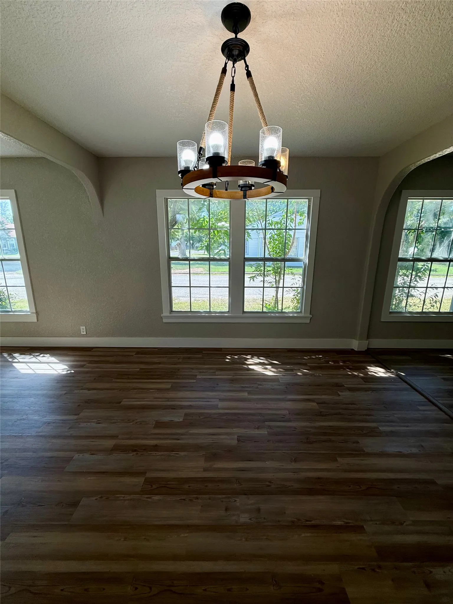 Spacious interior featuring wood-finish flooring, a contemporary chandelier, multiple windows, and arched wall openings