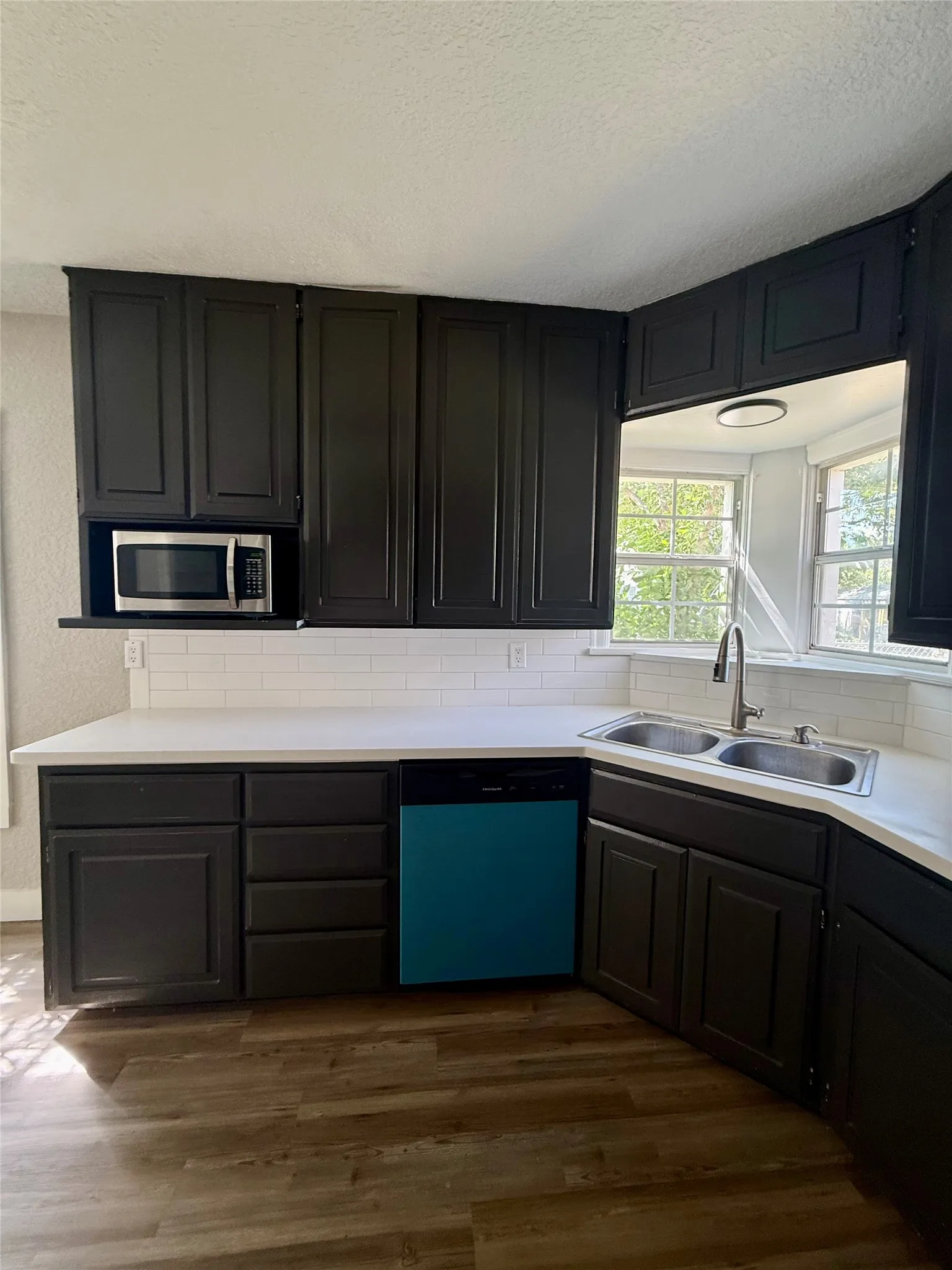 Kitchen featuring dark cabinetry, white countertops, subway tile backsplash, and wood-finish flooring