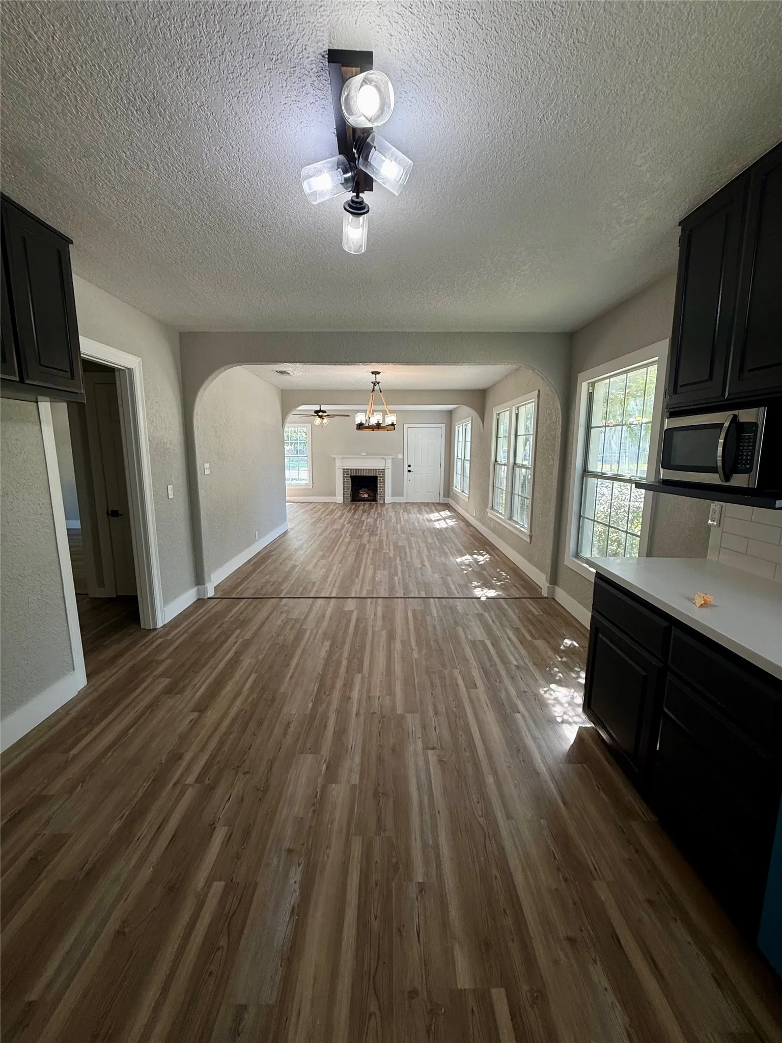 Expansive open-concept living area featuring wood-finish flooring, an arched doorway, and multiple windows