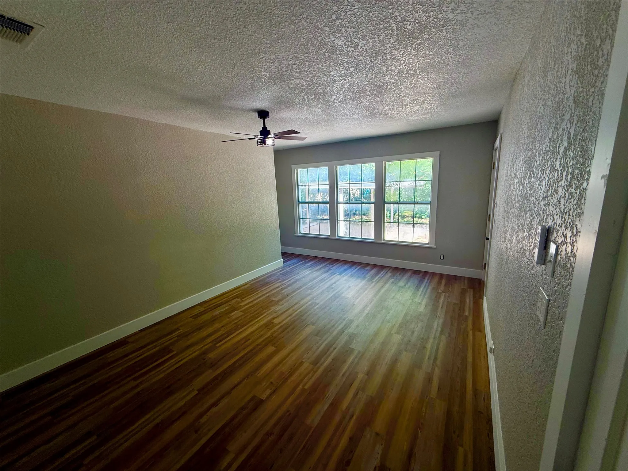 Middle primary bedroom Spacious room featuring wood-finish flooring, a contemporary ceiling fan, and a trio of large windows providing natural illumination