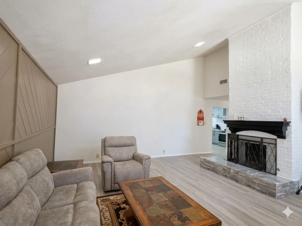 Vaulted ceiling living area featuring a white-painted brick fireplace with a dark wood mantel and a stone hearth