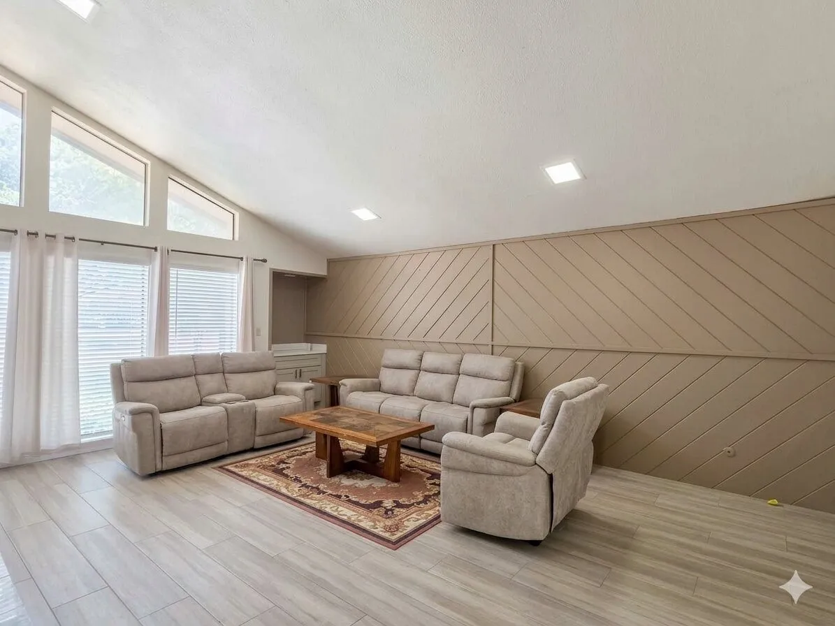 Spacious room featuring vaulted ceilings, wood-finish flooring, a built-in wet bar, a paneled accent wall, and large windows with transom architectural details