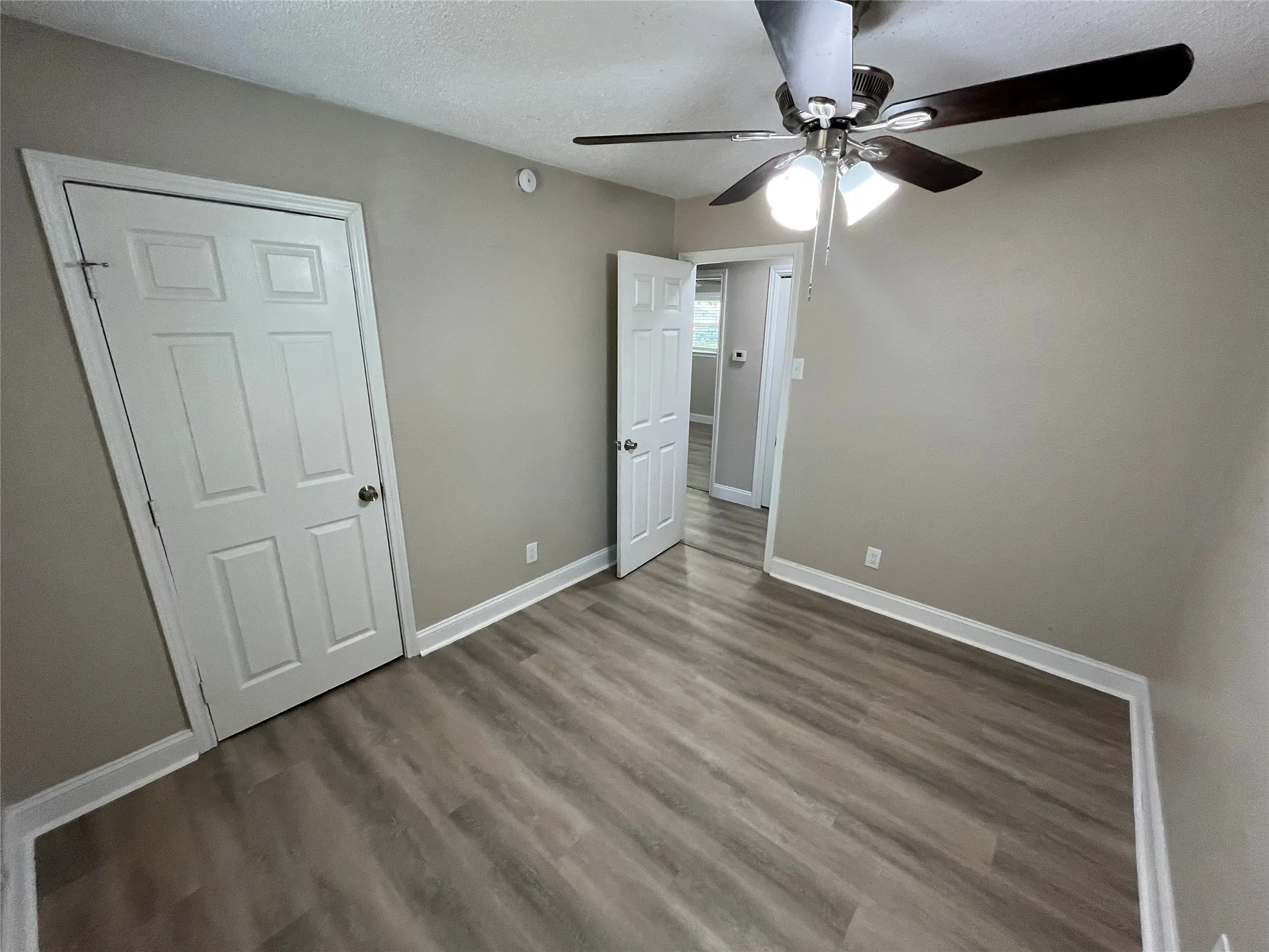 Room featuring wood-finish flooring, neutral wall paint, white trim, and a ceiling fan with integrated lighting