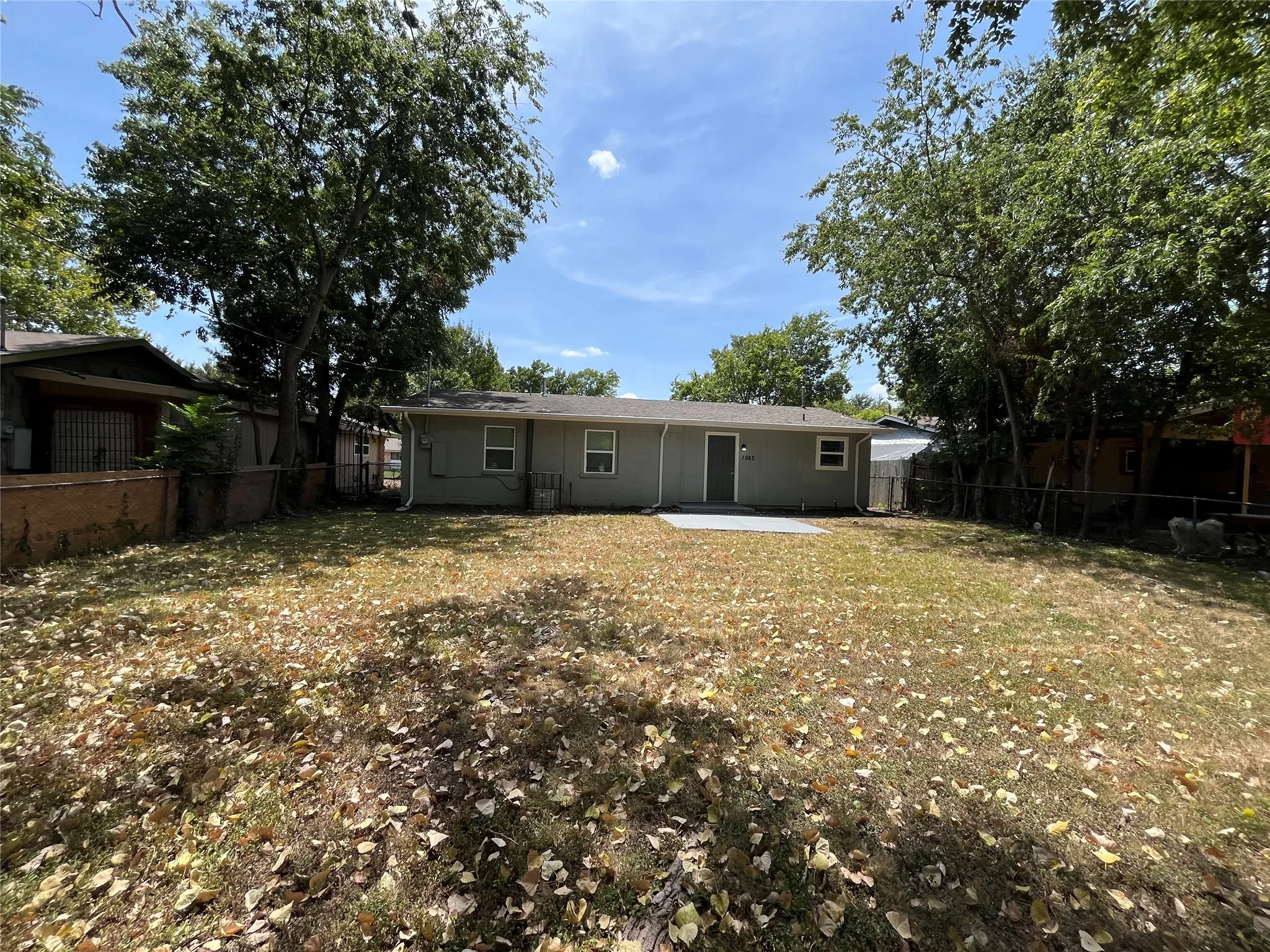 Expansive backyard featuring a large green space, mature trees, a concrete patio, and a light-colored exterior with multiple windows