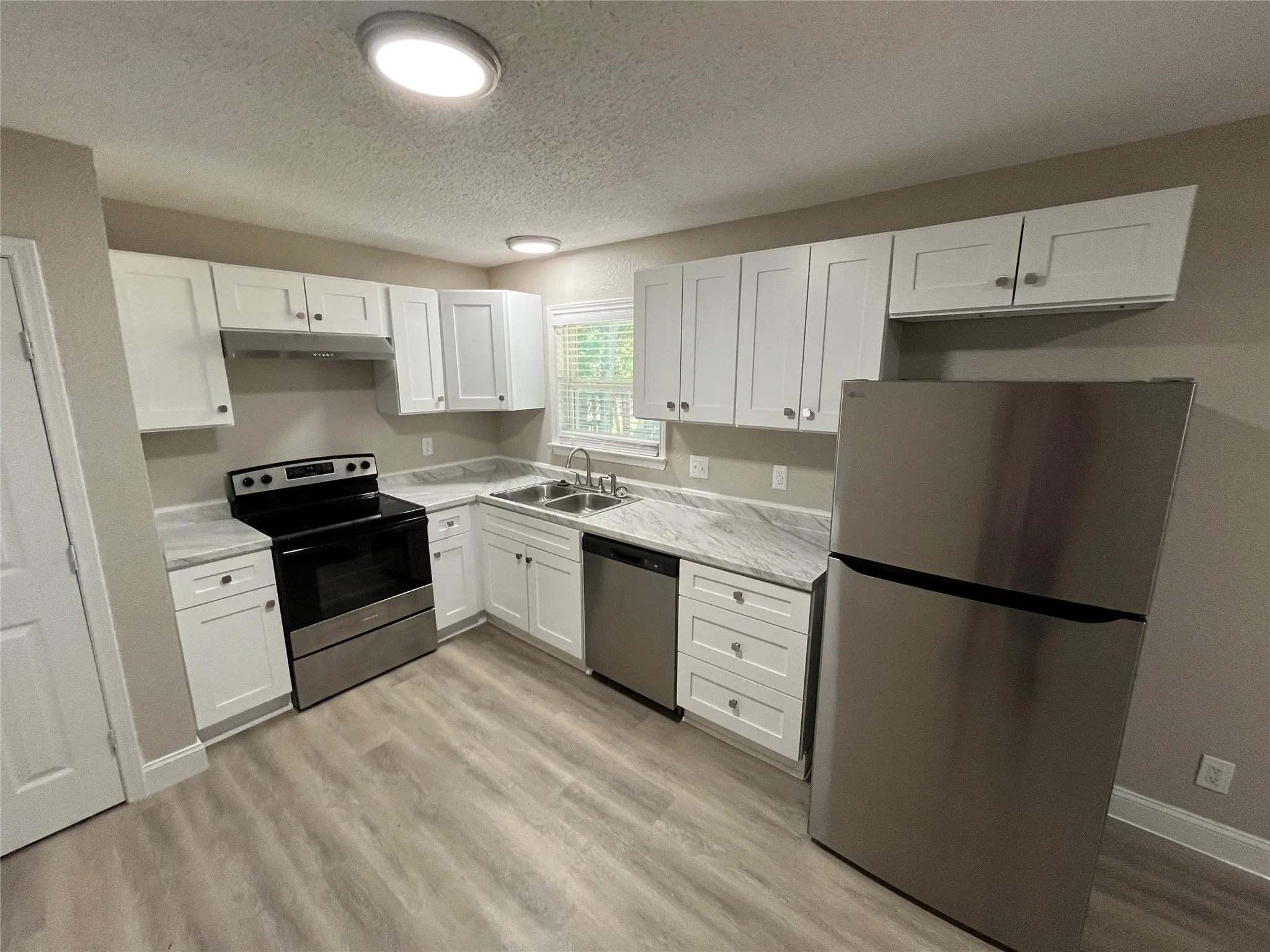 Kitchen featuring white shaker-style cabinetry with chrome hardware, marbled-finish countertops, and wood-finish flooring
