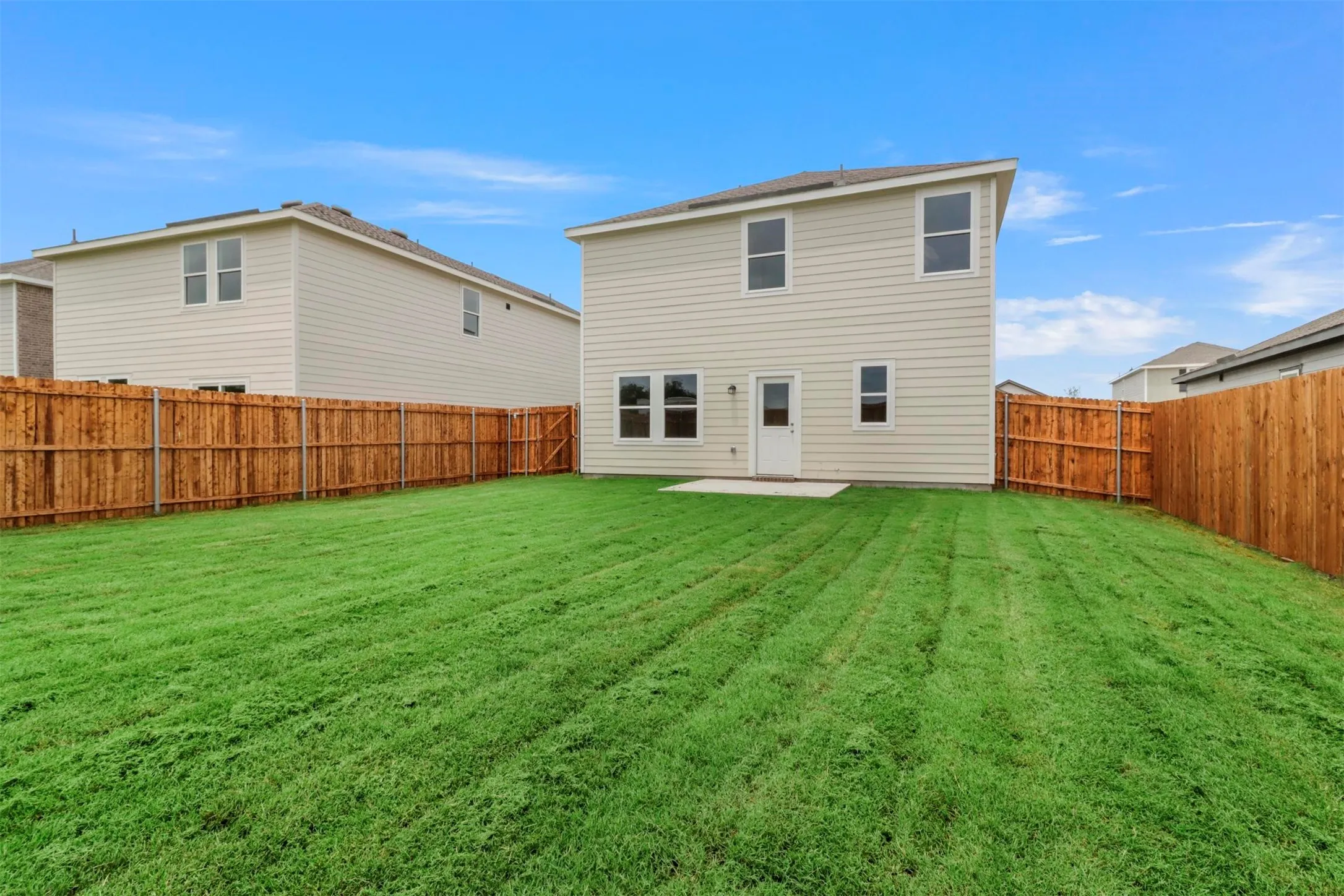 Expansive backyard featuring a lush green lawn, full privacy fencing, and a concrete patio