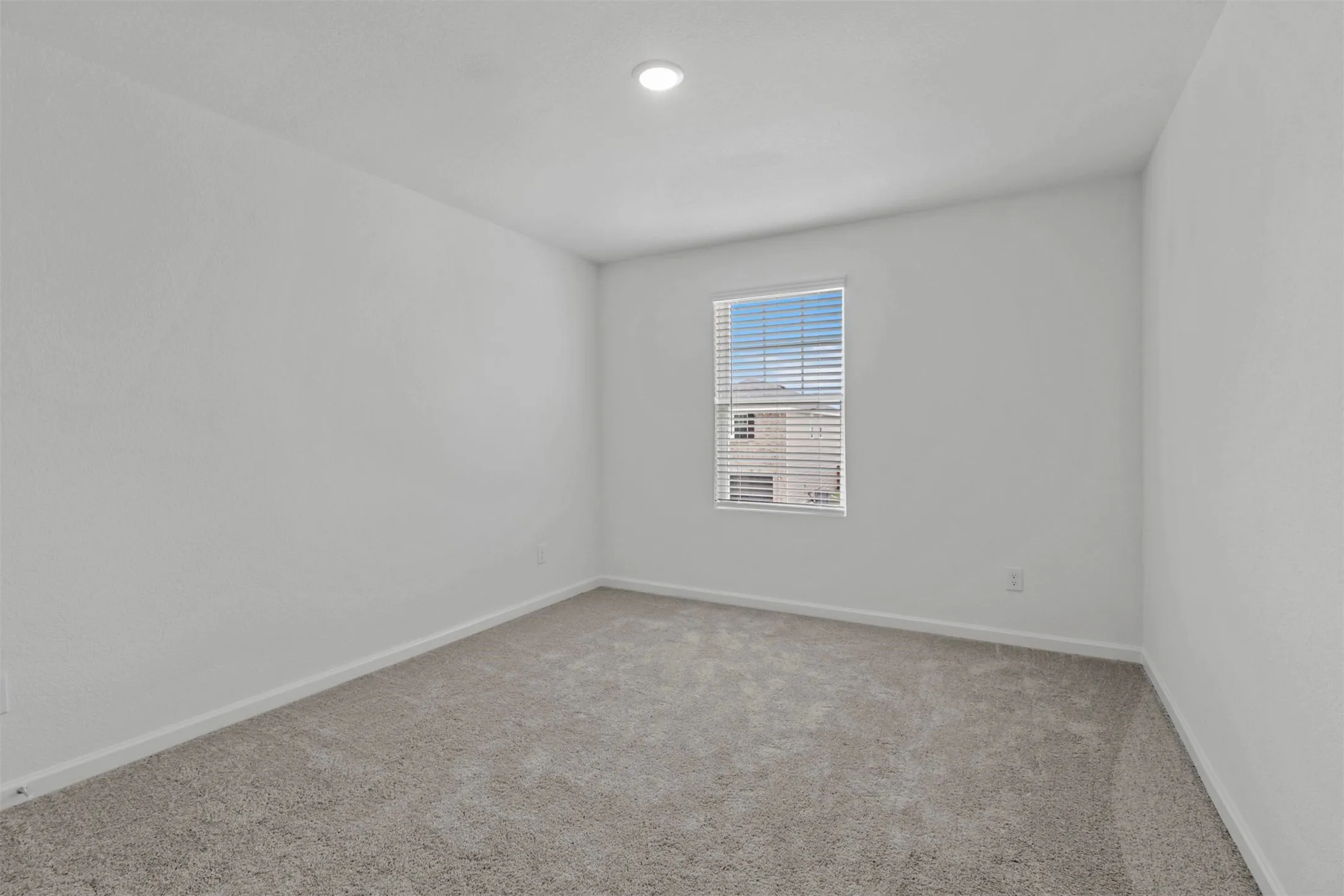 Carpeted room featuring a single window with blinds, white walls, white trim, and a recessed ceiling light