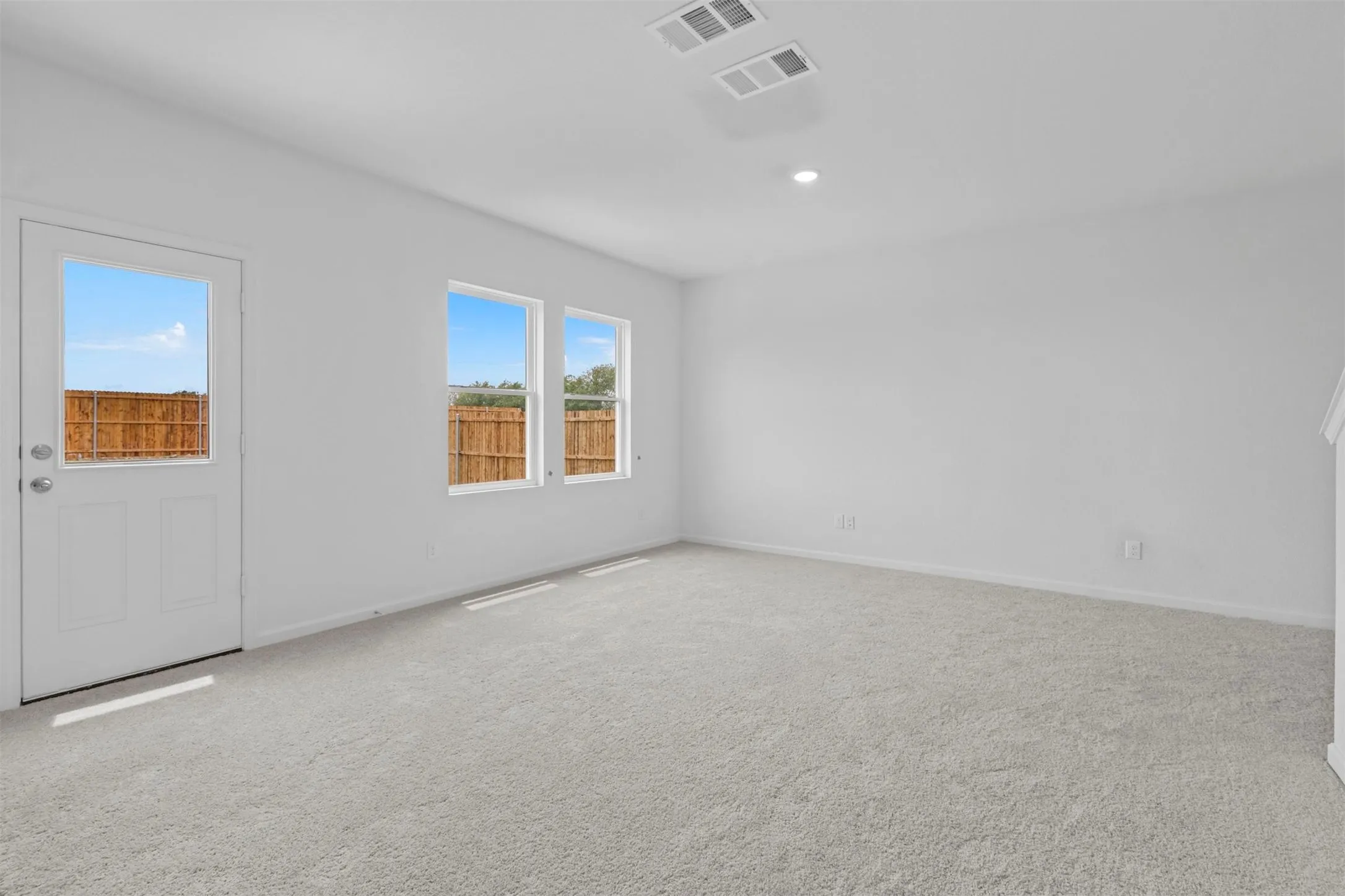 Spacious room featuring light-toned carpeting, white painted walls, and a full-light exterior door