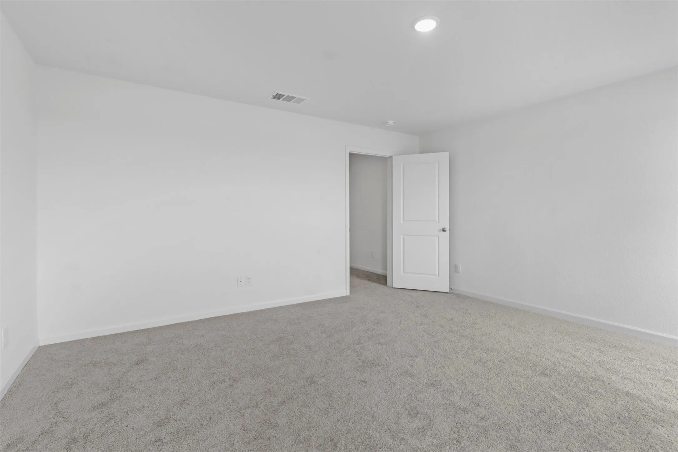 Spacious room featuring light gray carpeting, white walls, a single recessed ceiling light, and a white two-panel door
