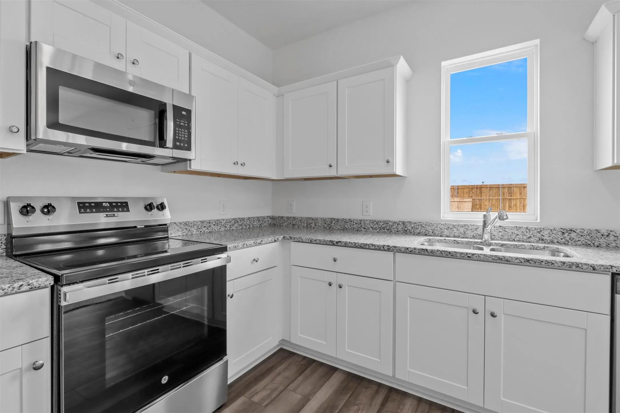 Kitchen featuring white cabinetry, speckled countertops, stainless steel appliances, and wood-finish flooring