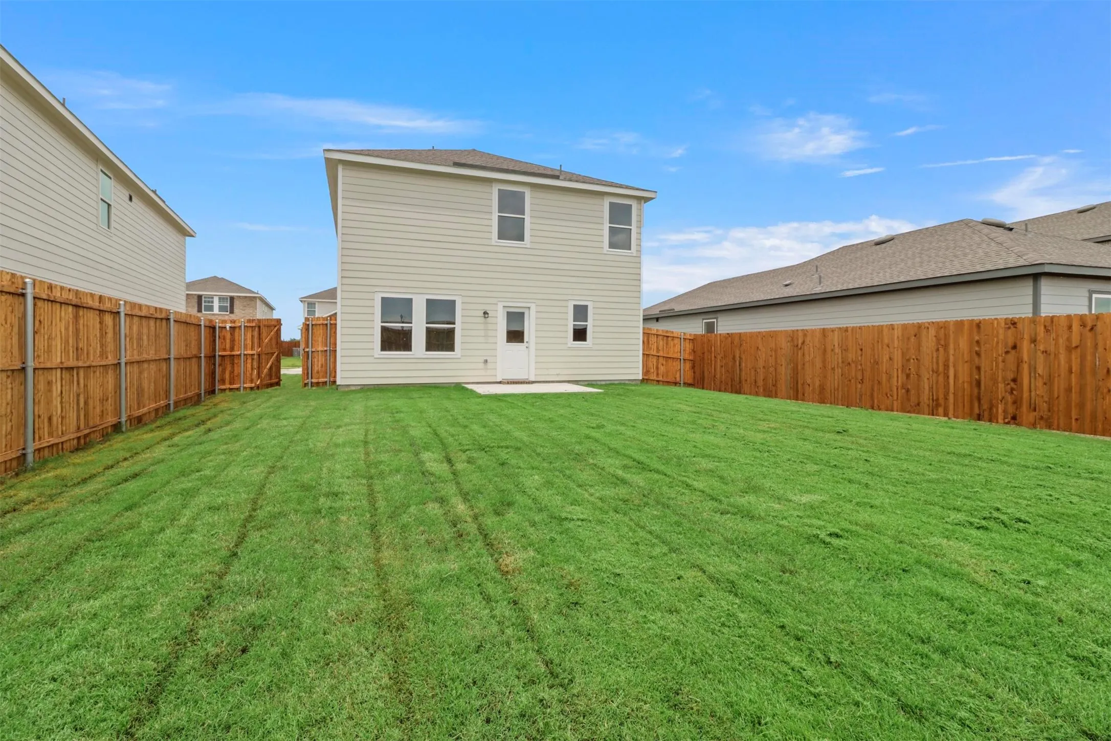 Spacious backyard featuring a large grass lawn, wood privacy fencing, and a concrete patio pad
