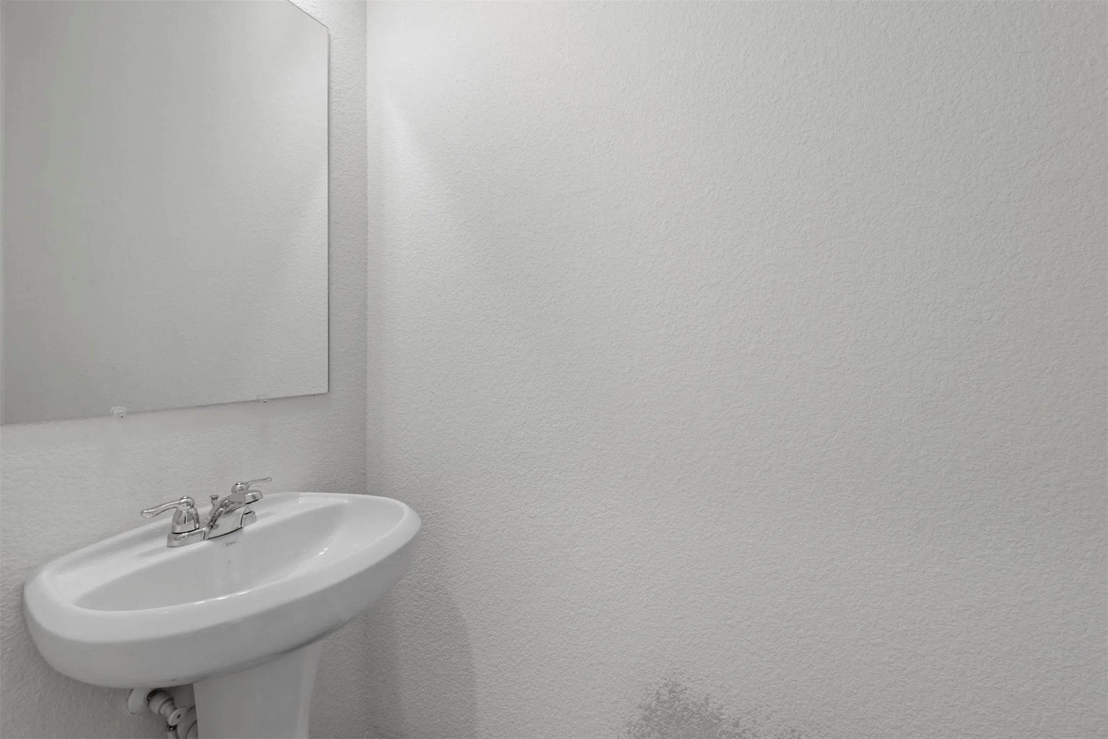 Pedestal sink with chrome faucet, framed by a wall-mounted mirror