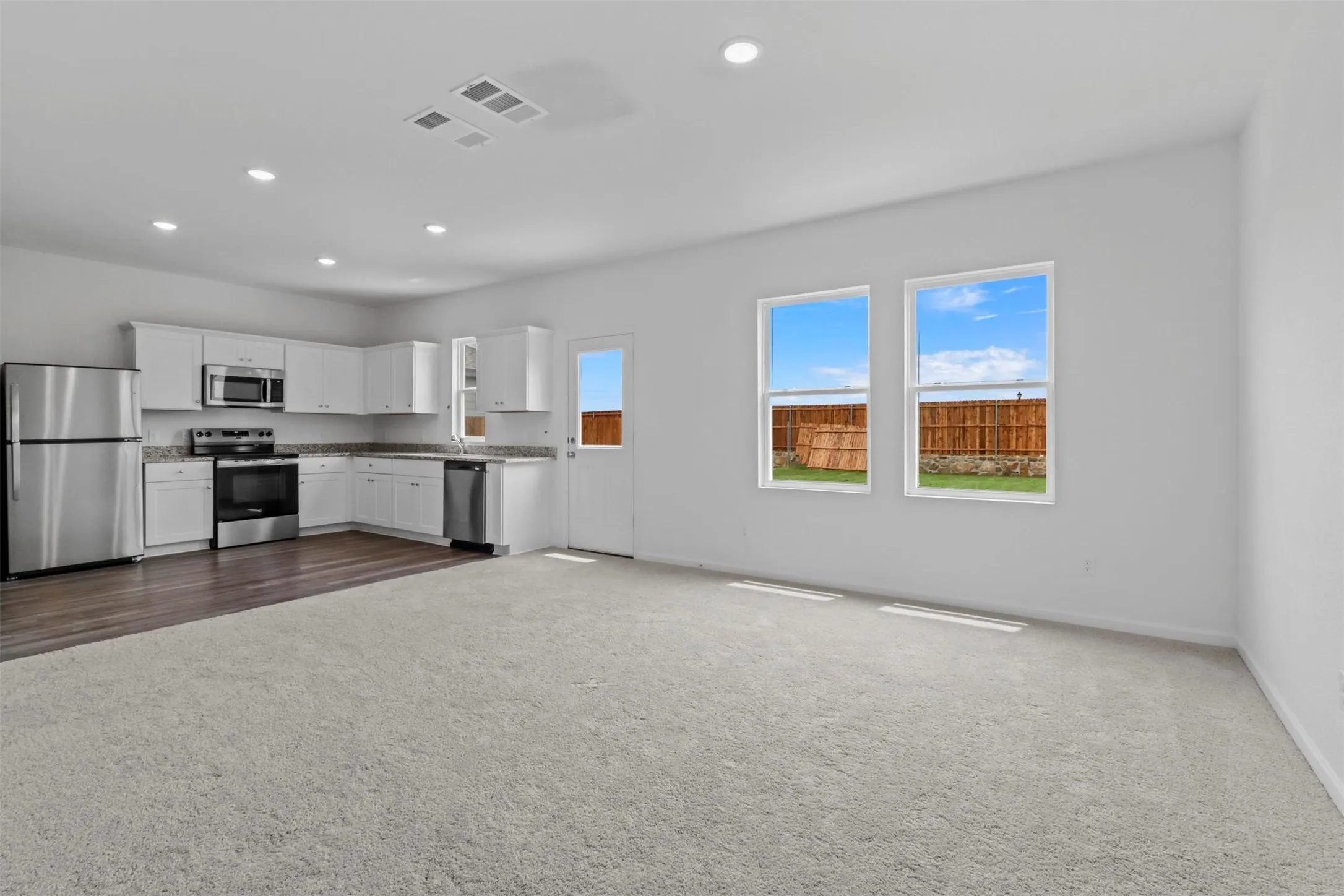 Open-concept living area featuring a kitchen with white cabinetry, stainless steel appliances, and wood-finish flooring