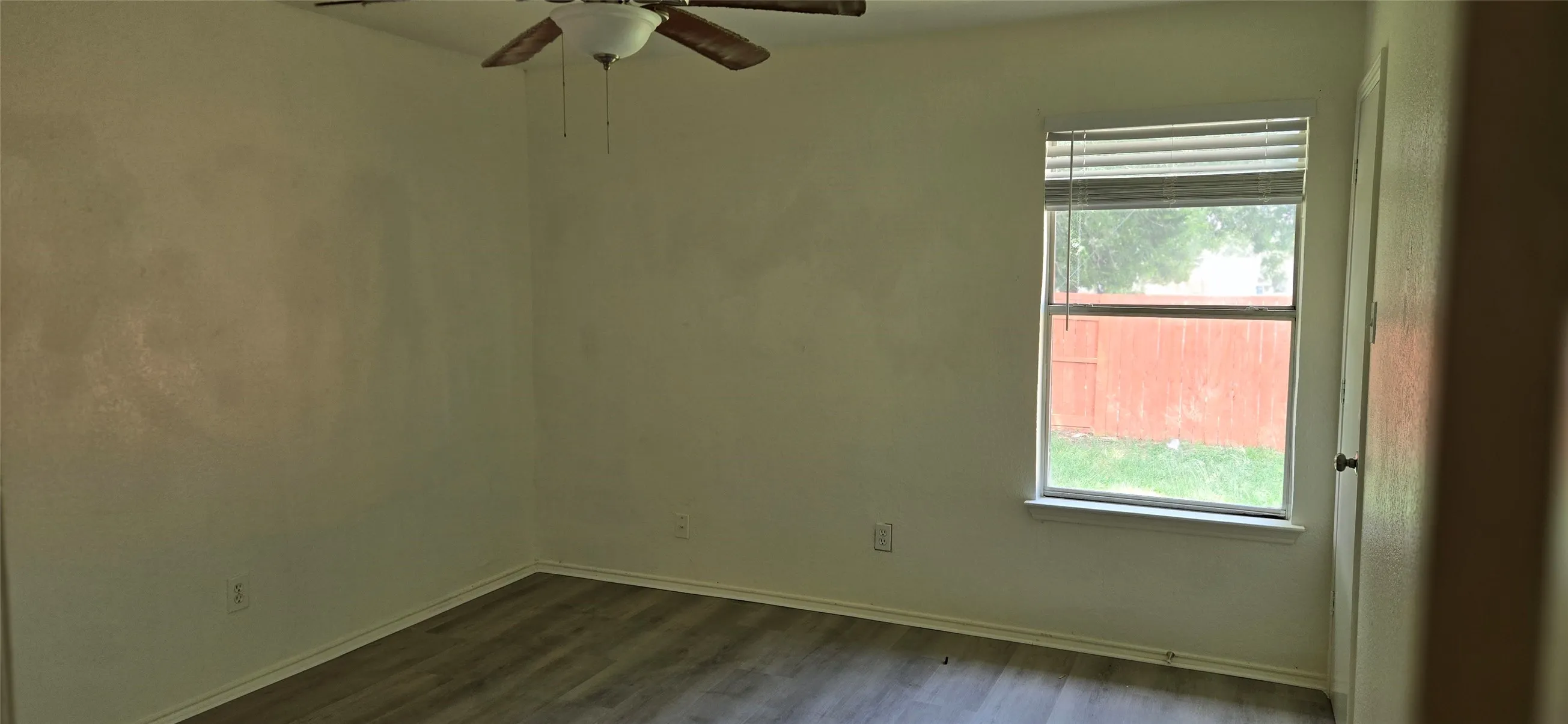 Interior space featuring wood-finish flooring, a ceiling fan with light fixture, and a window with blinds