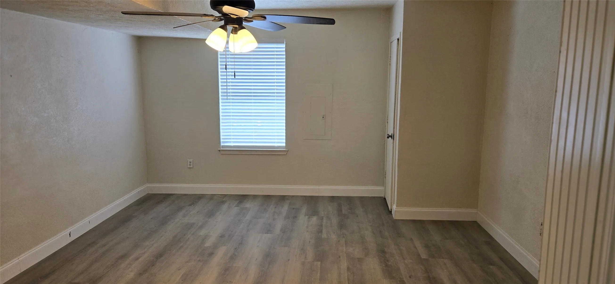 Room featuring wood-finish flooring, a window with blinds, a ceiling fan with integrated lighting, and a white trim package
