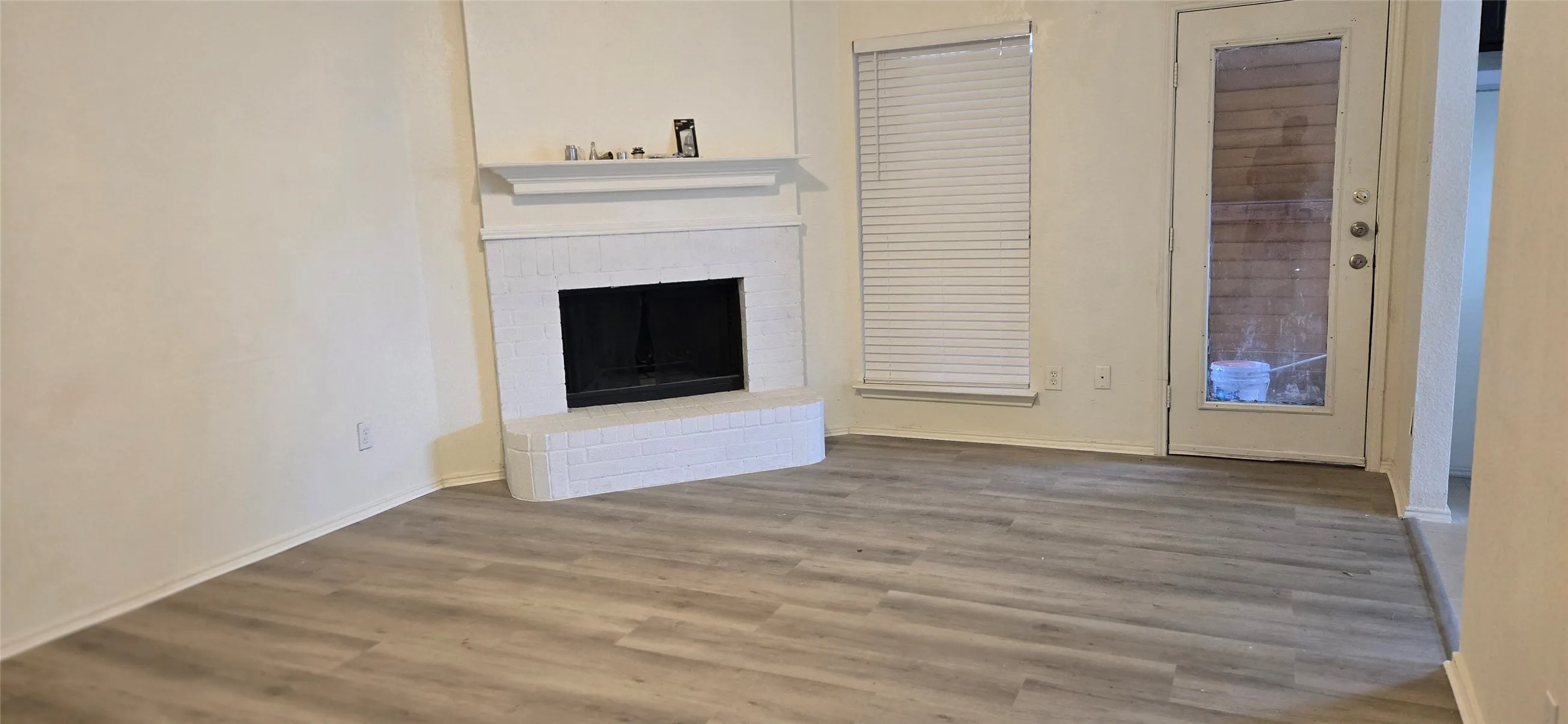 Living area featuring wood-finish flooring, a white brick fireplace with mantel, and a glass-paneled door