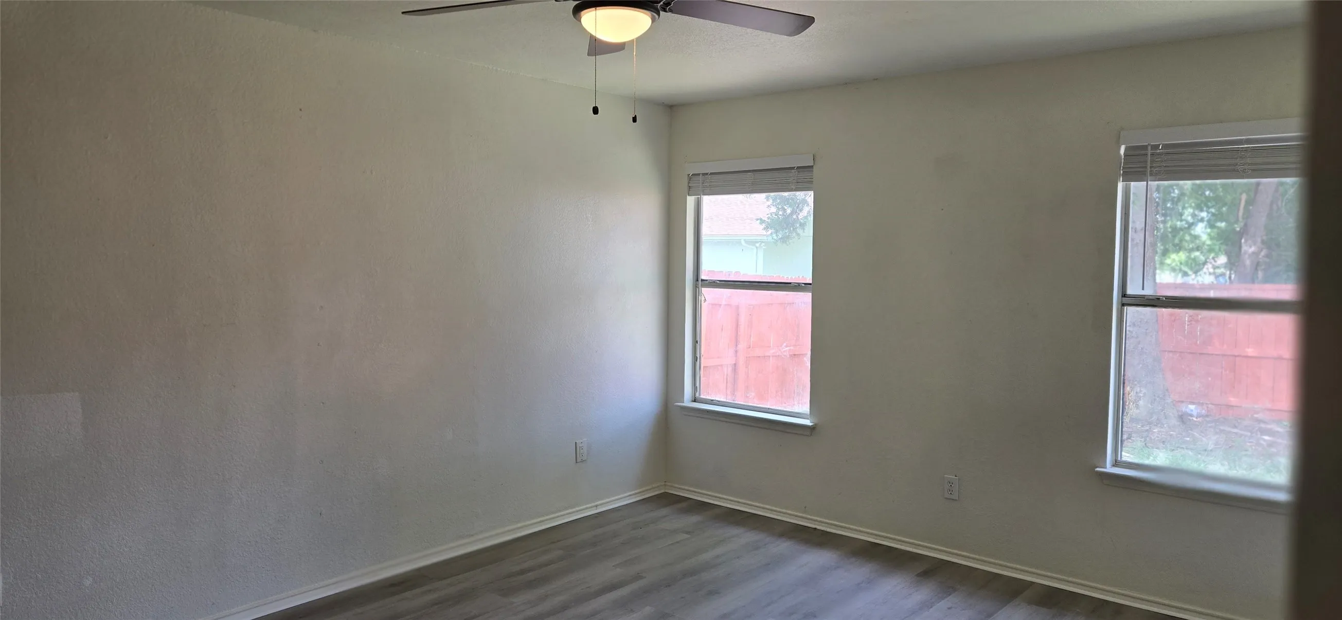 Room featuring two windows with blinds, a ceiling fan with integrated lighting, and wood-finish flooring