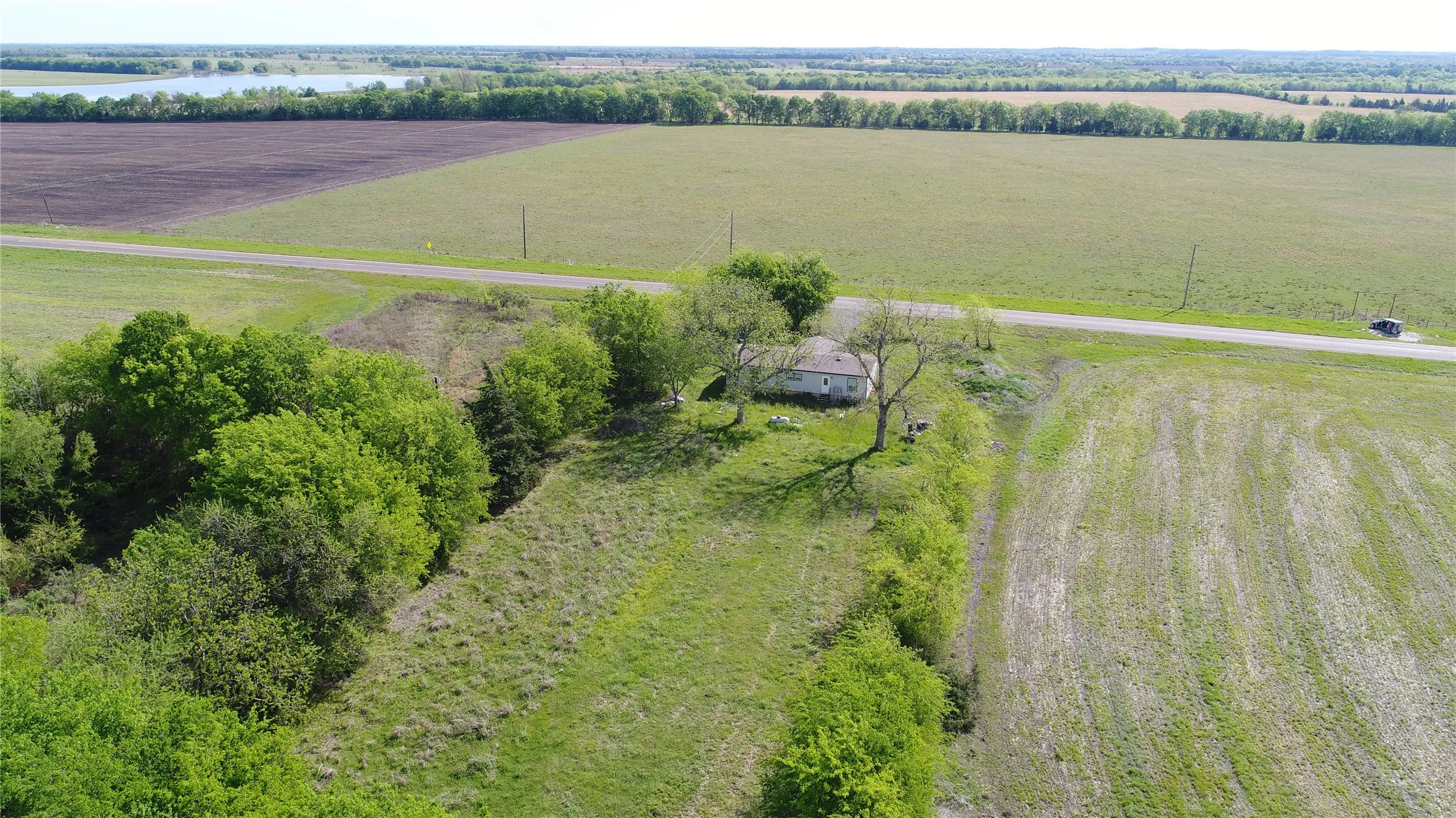 Rural property featuring a single-story residence, expansive green spaces, mature trees, and direct road frontage