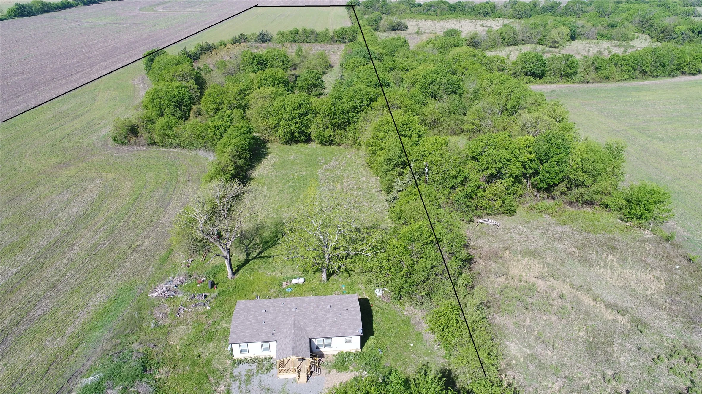 Rural property featuring a single-story dwelling, extensive natural landscaping, and surrounding cultivated fields