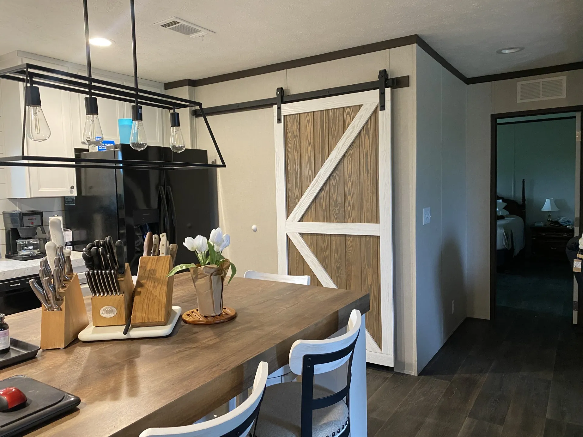 Kitchen featuring a large wood-finish island with seating, a contemporary linear chandelier, white cabinetry, and dark appliances