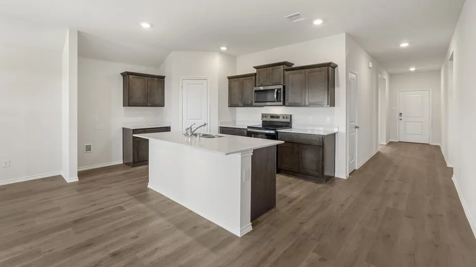 Modern kitchen featuring a central island with an integrated sink, dark wood-finish cabinetry, stainless steel appliances, and light-toned countertops