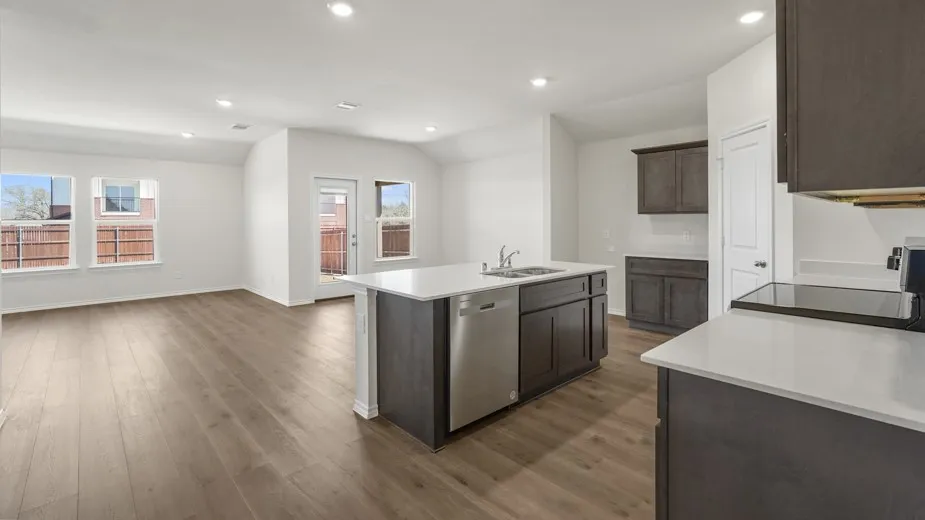 Integrated kitchen and living area featuring wood-finish flooring, recessed lighting, and ample natural light through multiple windows and a glass-paneled door