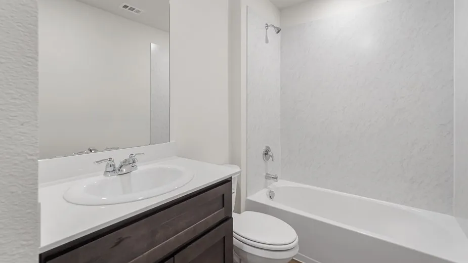 Bathroom featuring a white vanity countertop, undermount sink, dark wood-finish cabinetry, a framed mirror, and a white tub with textured surround