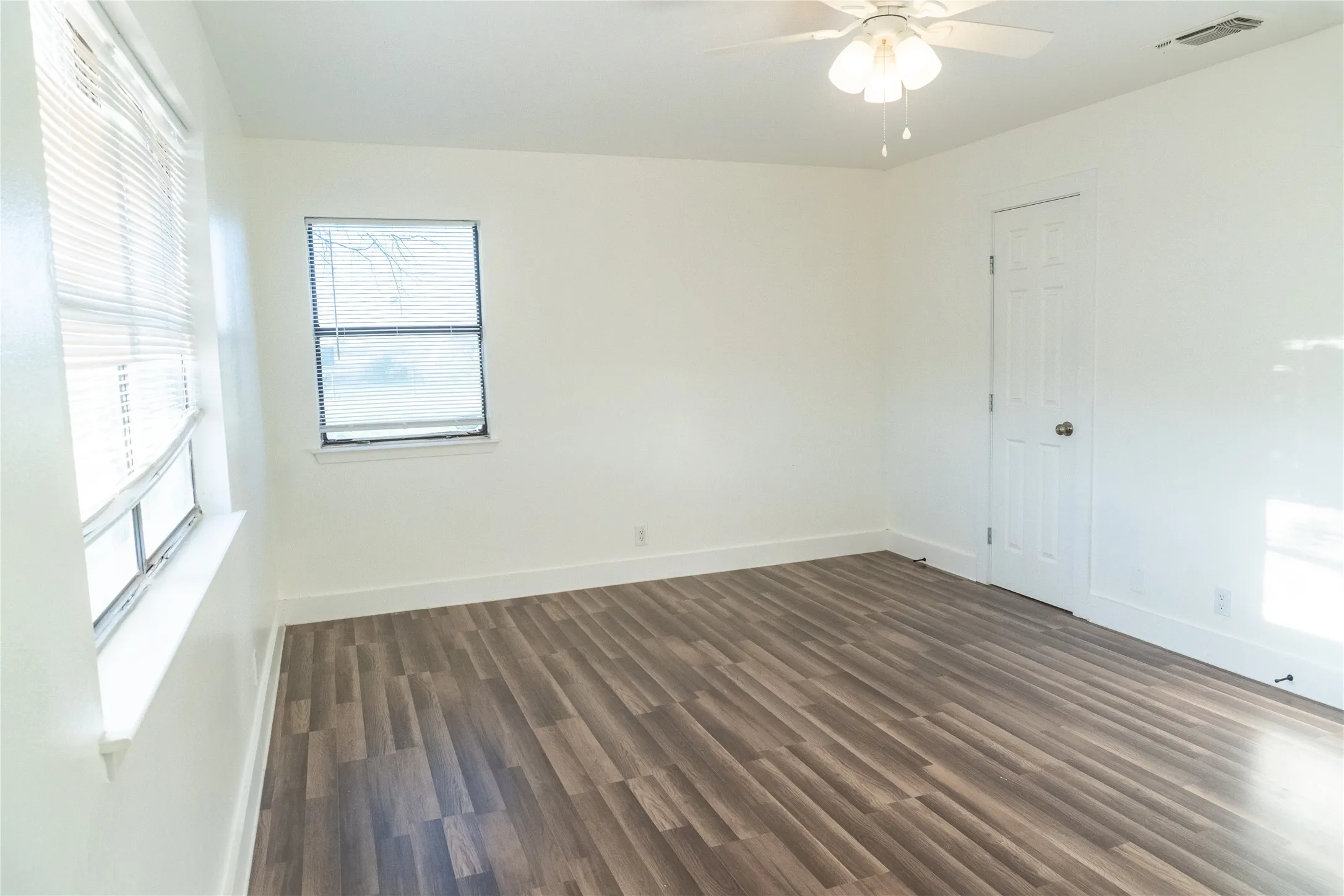 Spacious room featuring wood-finish flooring, white walls, and bright white trim