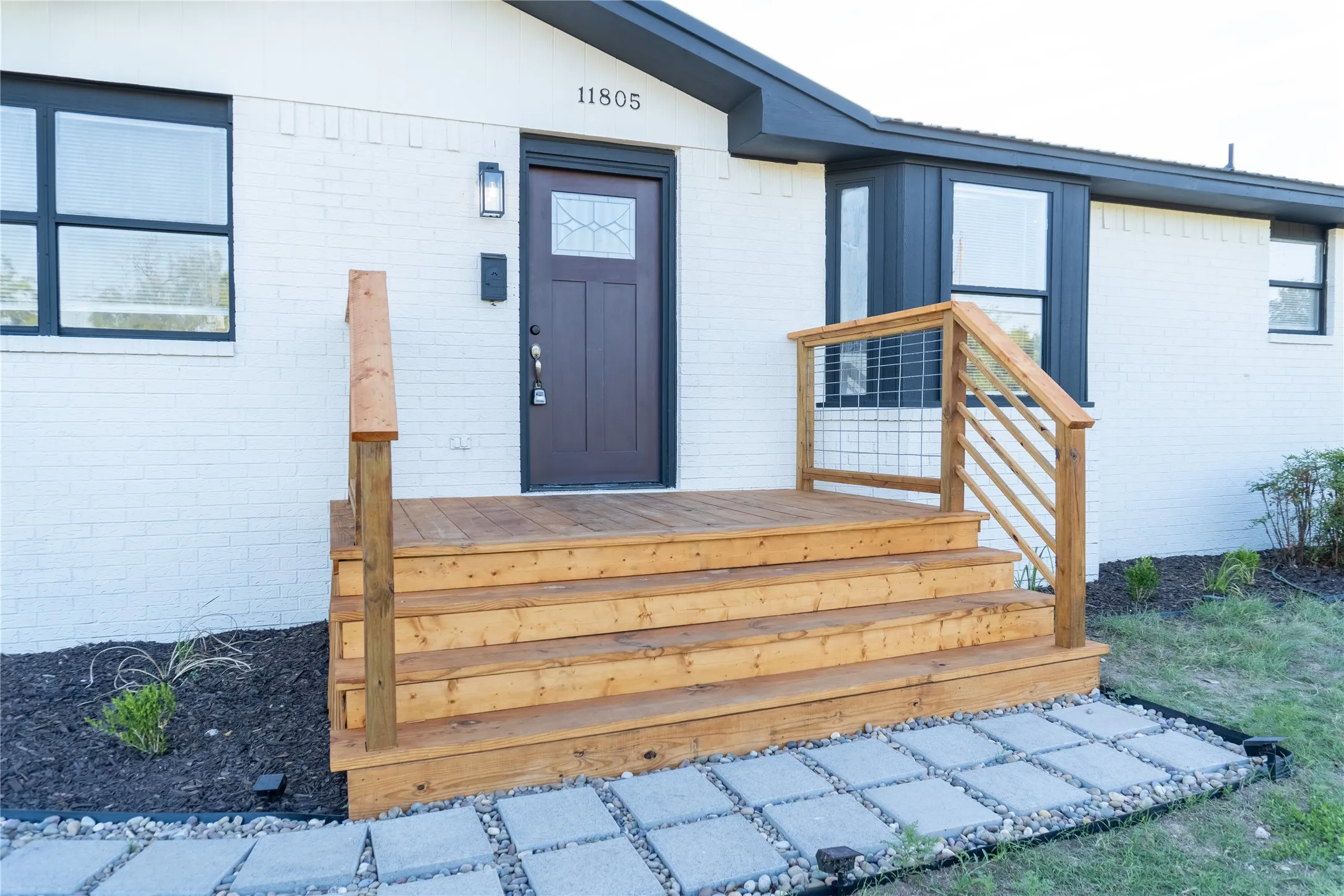 White brick exterior with dark trim accents, a wood-finish front porch, and a dark entry door with decorative glass