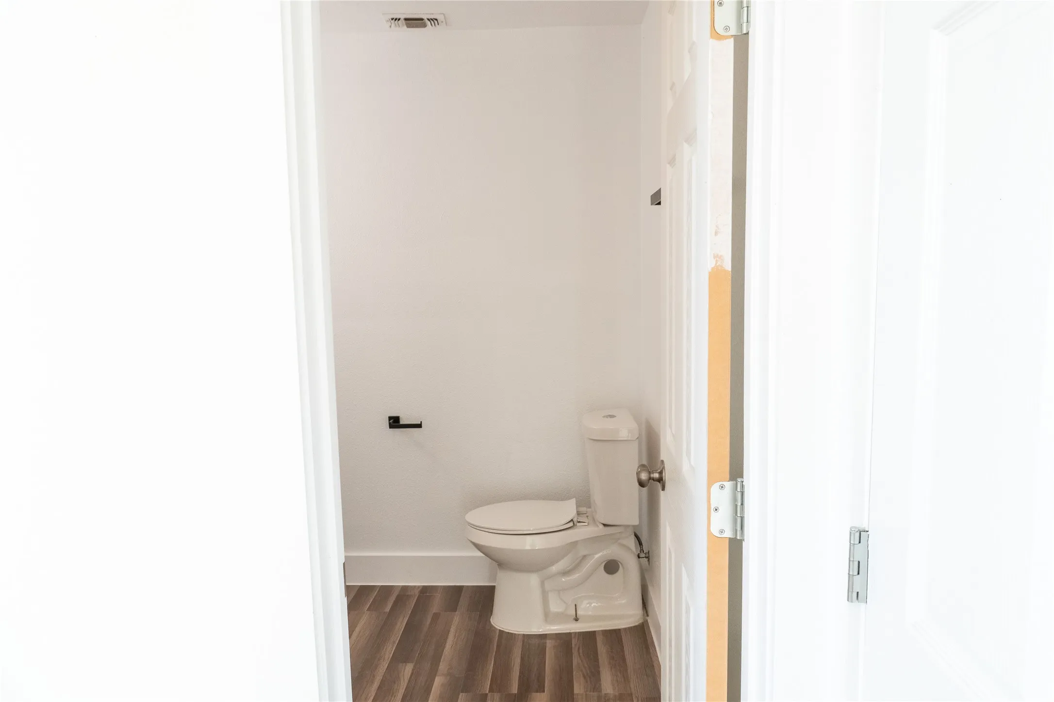 Compact powder room featuring a single toilet, wood-finish flooring, and crisp white walls