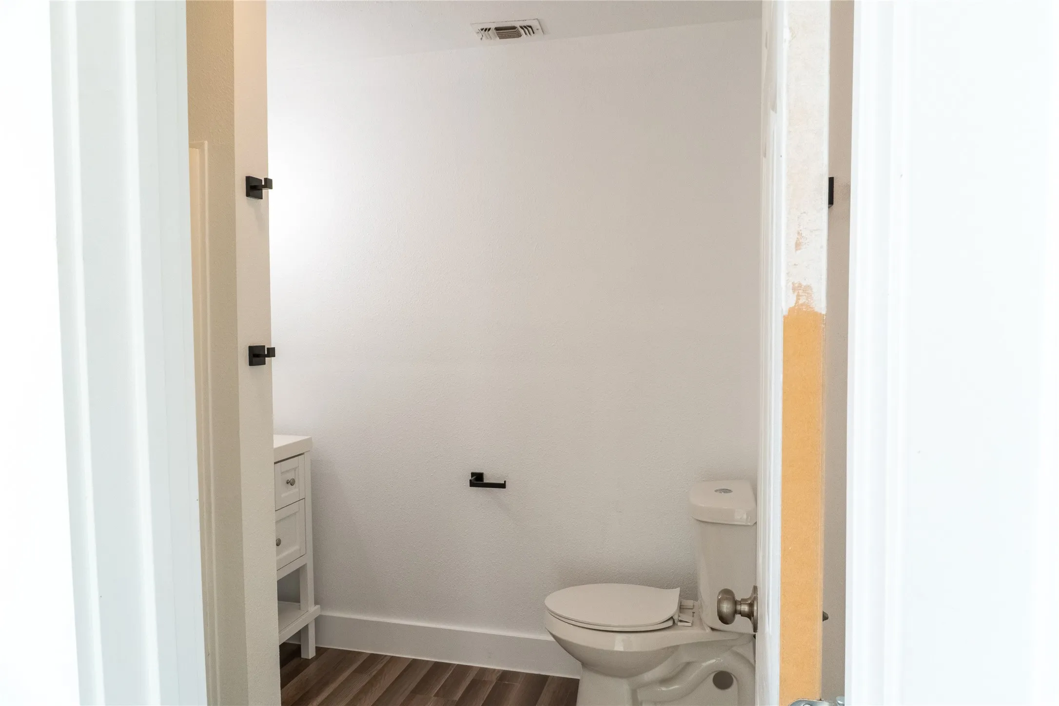Powder room featuring a white single vanity with storage, a standard white toilet, wood-finish flooring, and matte black hardware