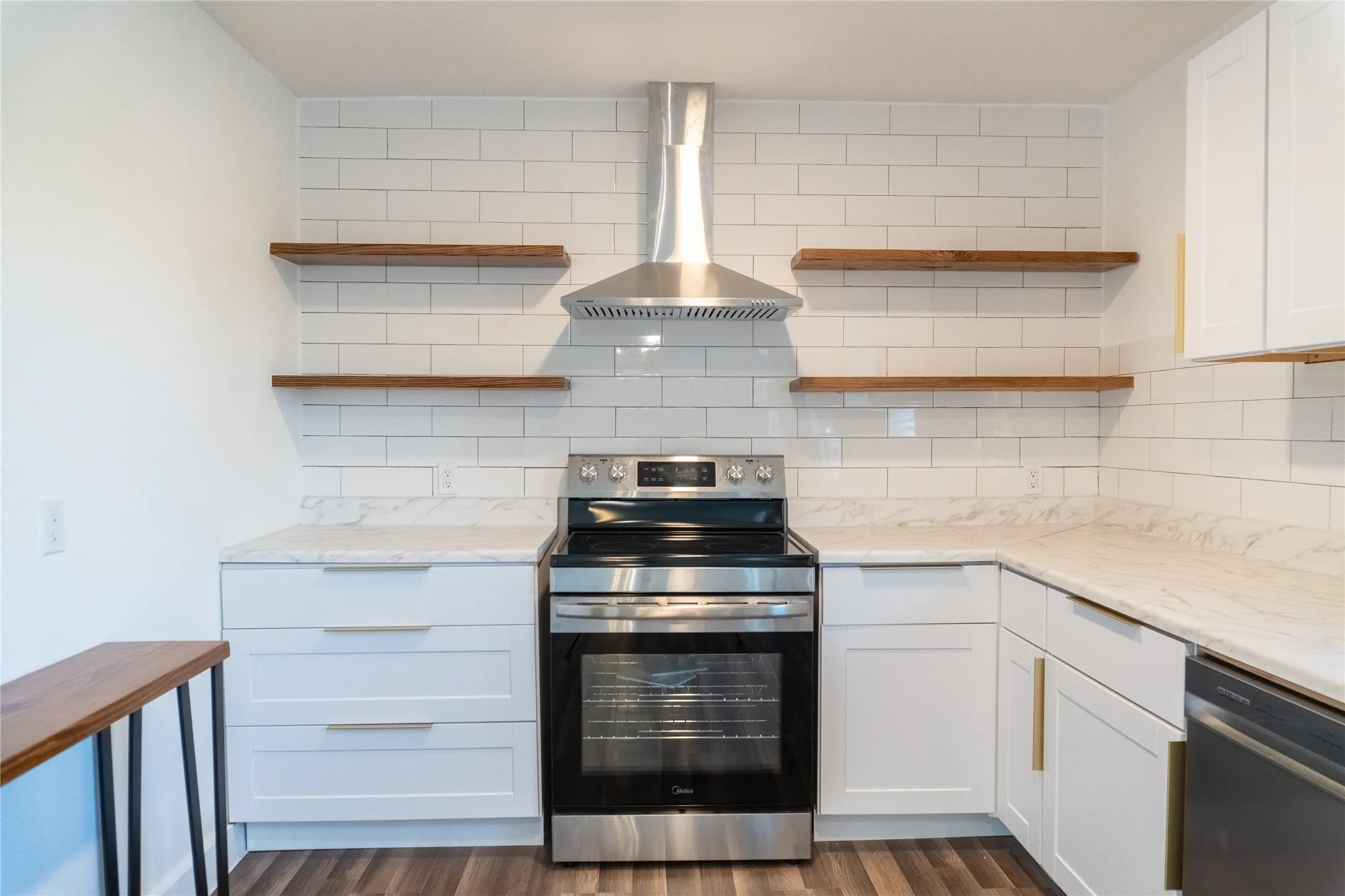 Kitchen featuring a stainless steel range with a coordinating range hood, white subway tile backsplash, white cabinetry with gold-tone hardware, and wood-finish flooring