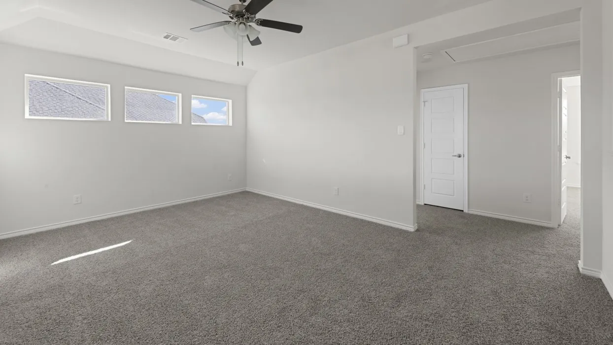 Spacious room featuring gray carpeting, light-colored walls, and a tray ceiling with a ceiling fan