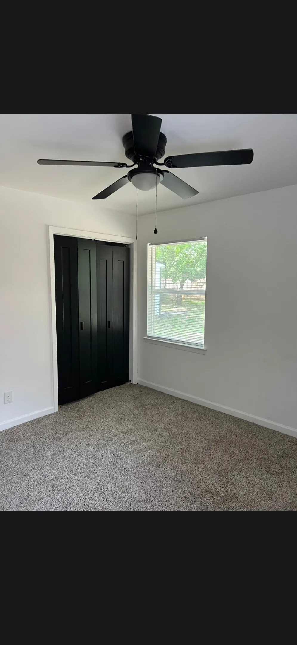 Carpeted room featuring a ceiling fan with integrated lighting, a window with a white frame, and dark bi-fold closet doors
