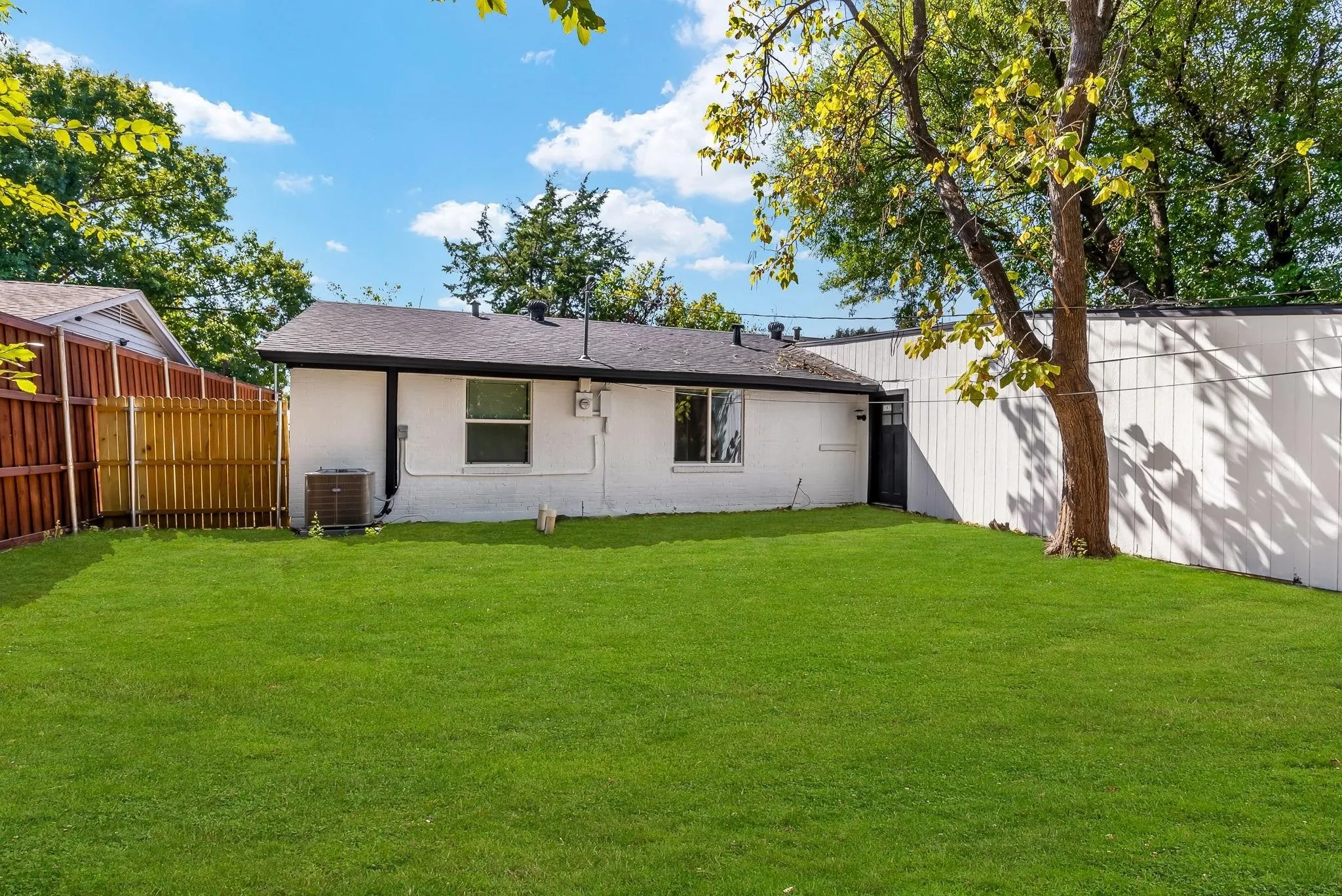 Expansive backyard featuring a manicured lawn, a privacy fence, and mature trees