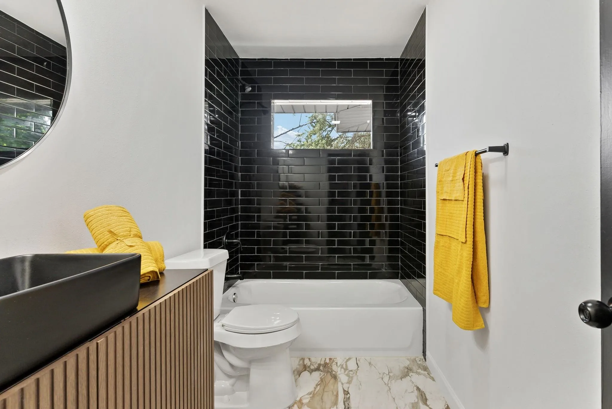 Bathroom featuring a deep-set tub with black subway tile surround, a rectangular window, and a wall-mounted vanity with a black vessel sink