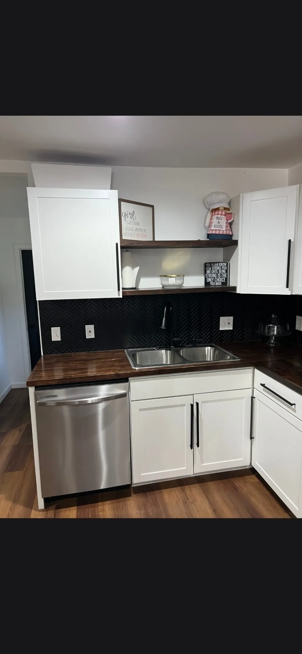 Kitchen featuring wood-finish countertops, a double stainless steel sink with a matte black faucet, and white shaker-style cabinetry with black pulls