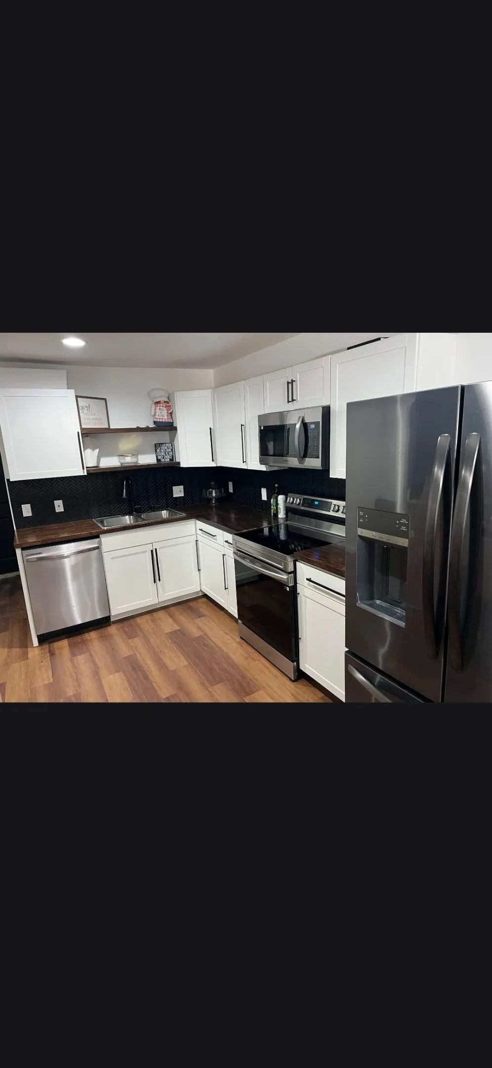 Modern kitchen featuring white cabinetry with dark hardware, dark countertops, and wood-finish flooring