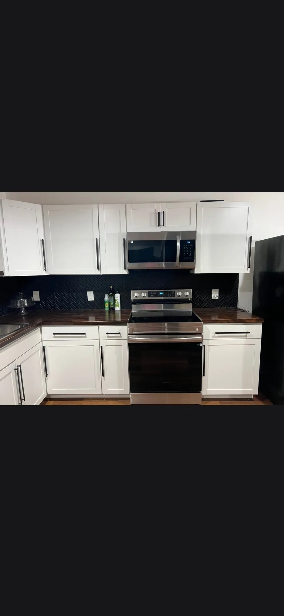 Modern kitchen featuring white cabinetry with dark hardware, dark countertops, a dark tile backsplash, and stainless steel appliances including a range and over-the-range microwave