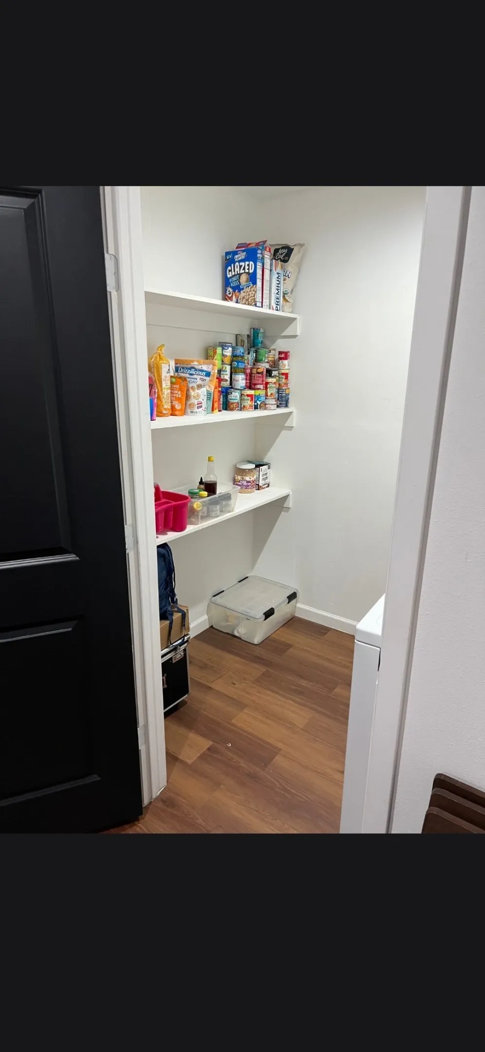 Walk-in pantry featuring white shelving, light neutral walls, and wood-finish flooring