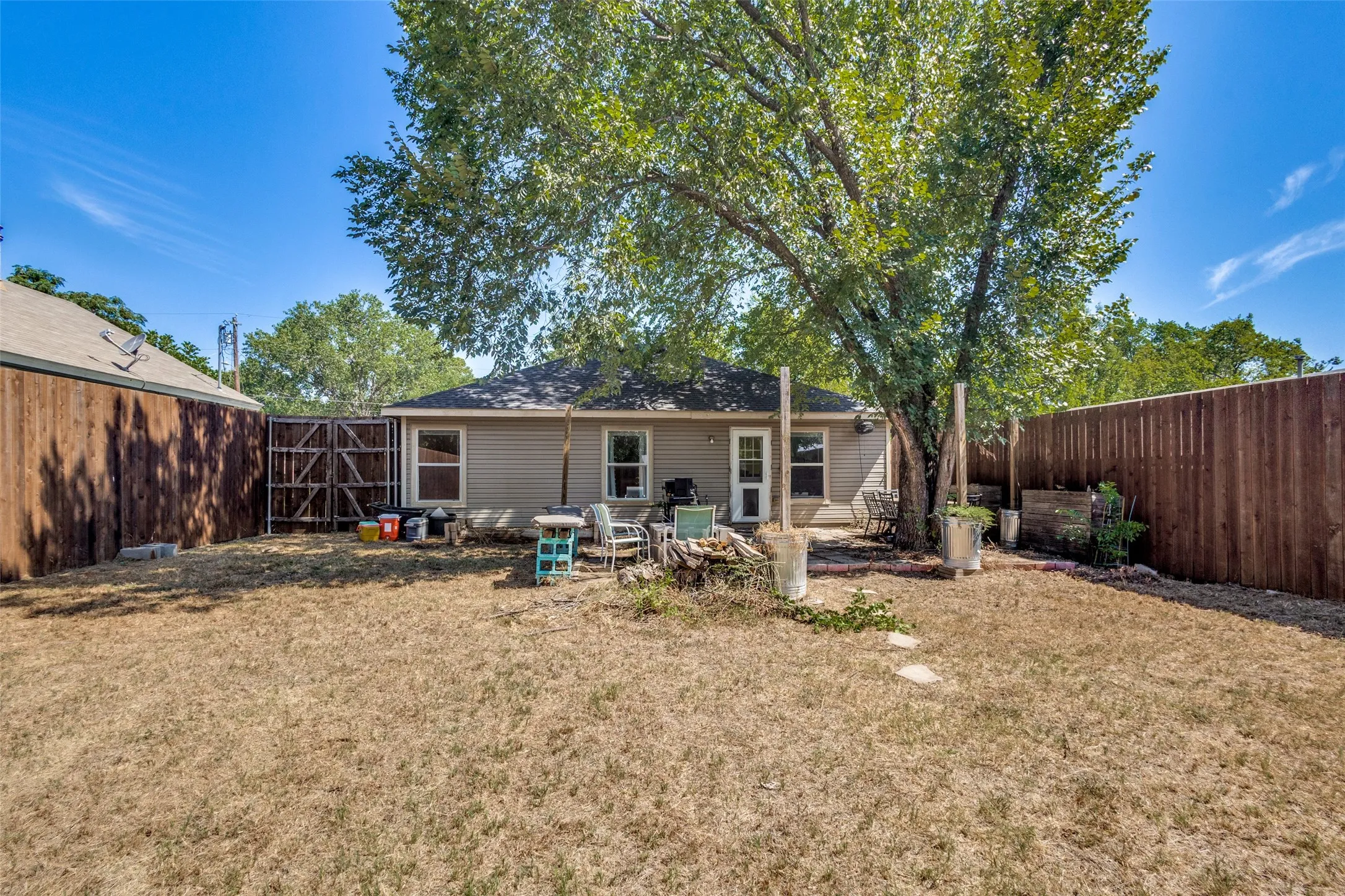 The backyard has a large tree that provides shade for the home and patio.