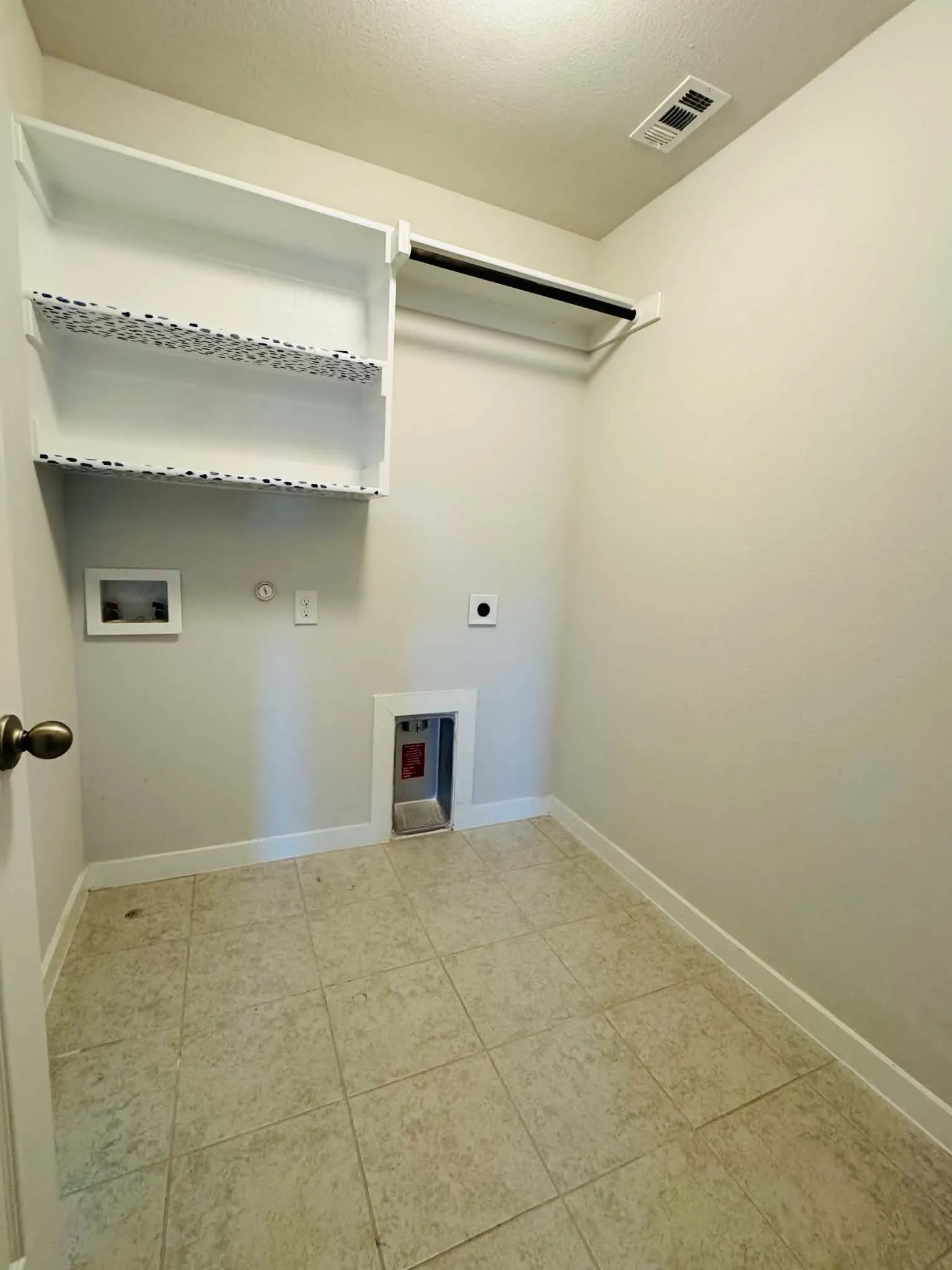 Dedicated utility space featuring tile flooring, white baseboards, wall-mounted shelving, and a hanging rod